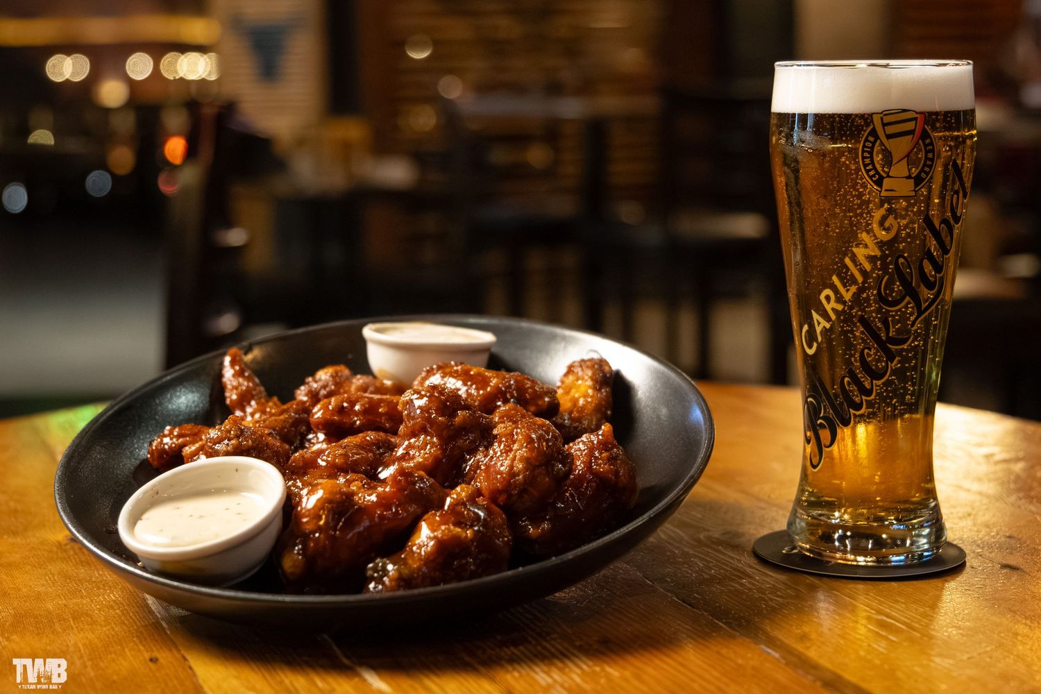 Beer glasses and BBQ dishes on dark wooden table in restaurant ambiance.