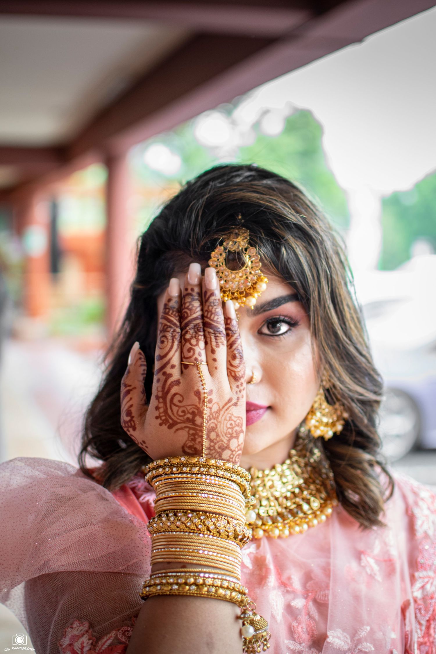 Close-up of intricate henna designs on hands with traditional Indian bridal jewelry and pink outfit.