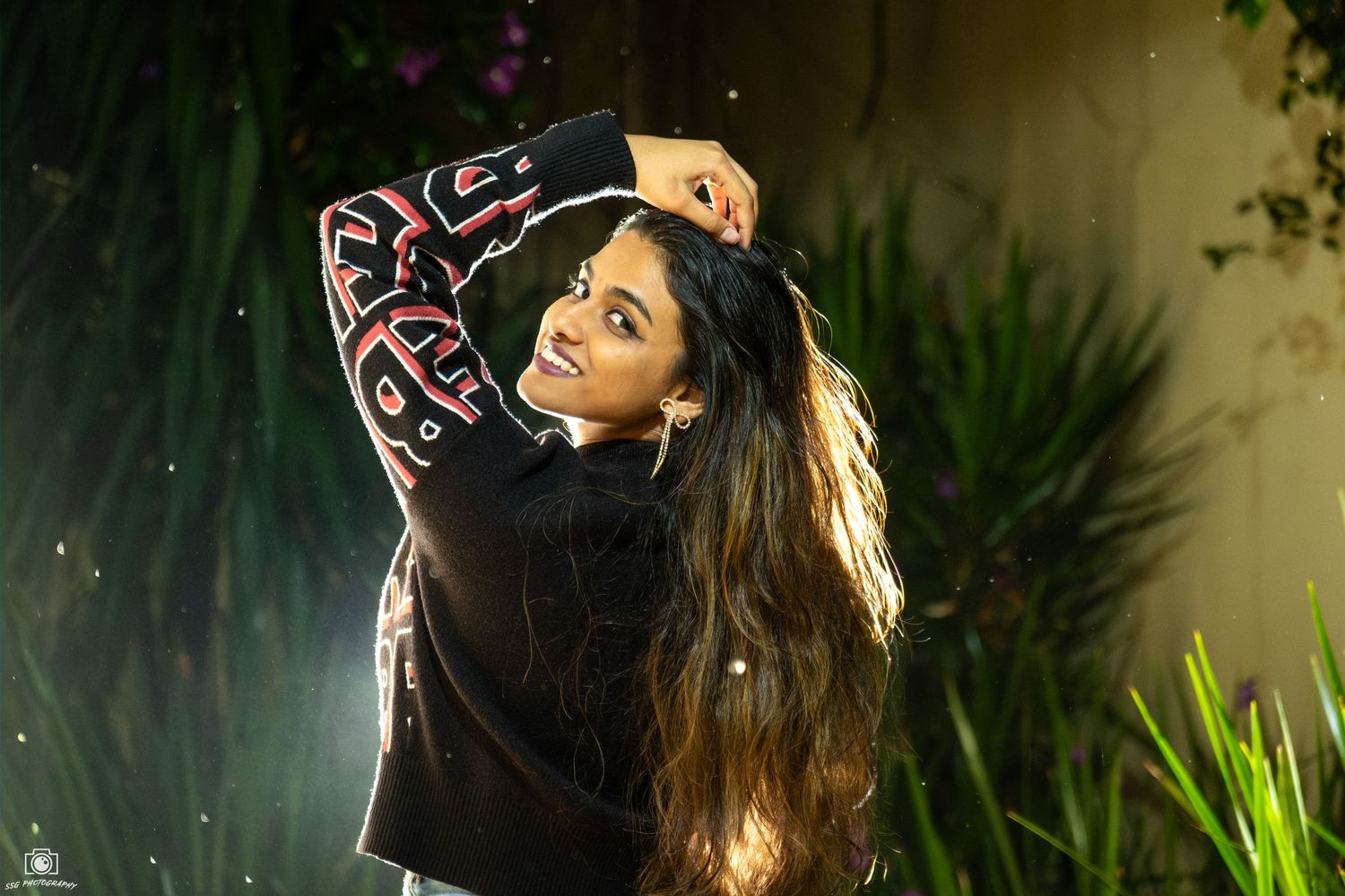 Dramatic evening photoshoot with someone wearing a black top with red lettering in a garden setting.