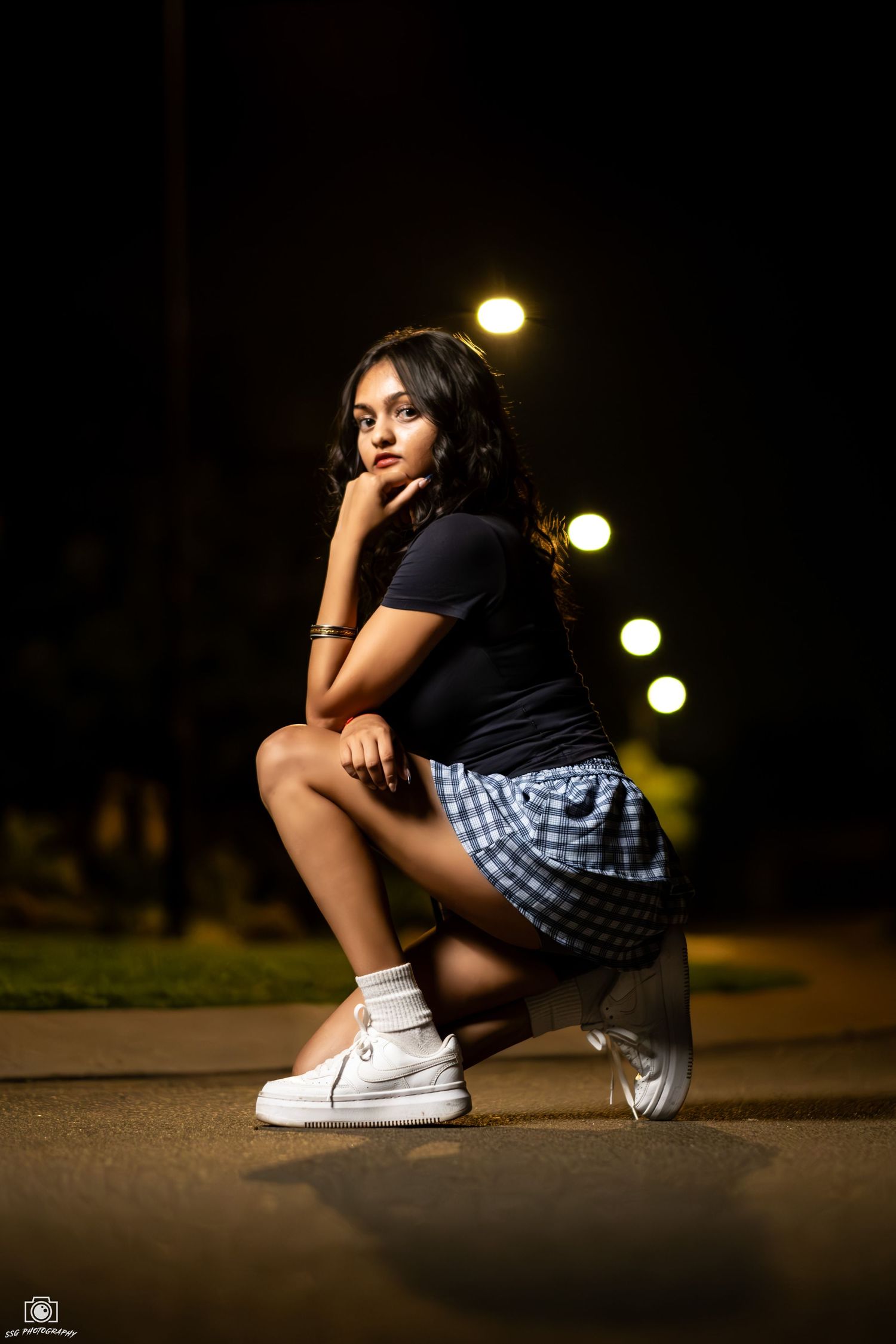 Dramatic nighttime portrait series showing someone crouched in casual wear with white sneakers under street lights.