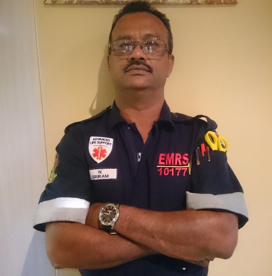 Emergency medical responder in a navy uniform with EQRS patch stands with crossed arms in a professional pose.