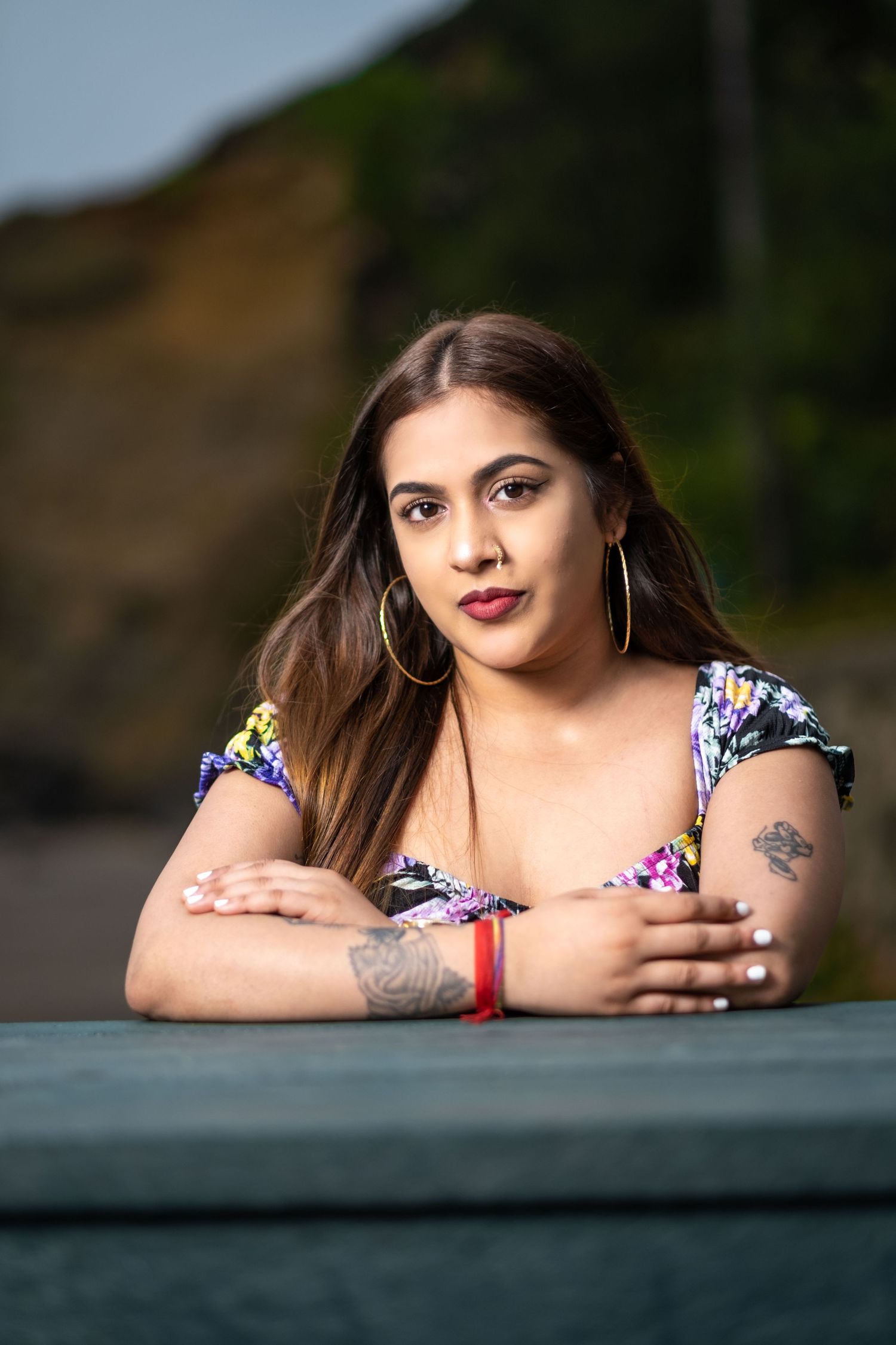 Woman in floral print top poses casually on a dark surface in an outdoor portrait series.