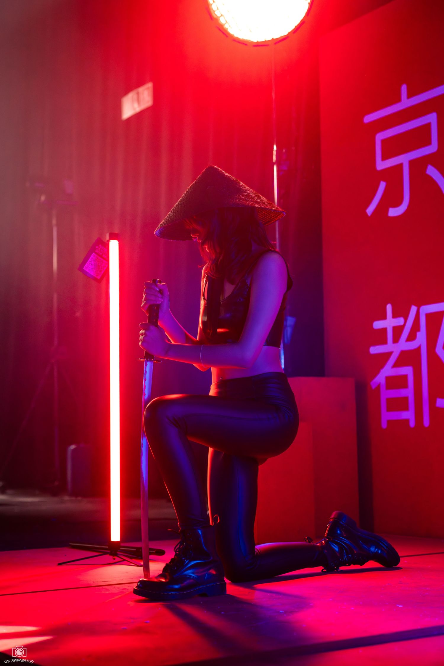Dramatic red-lit studio scene with figure seated against wall with Asian characters.
