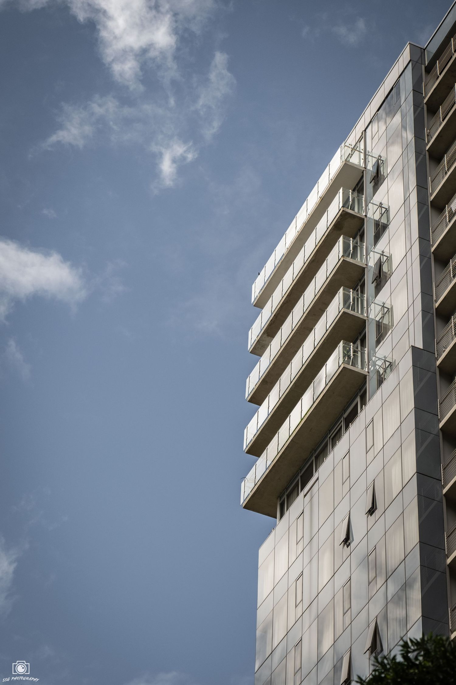 Modern glass building exterior with balconies against blue sky.