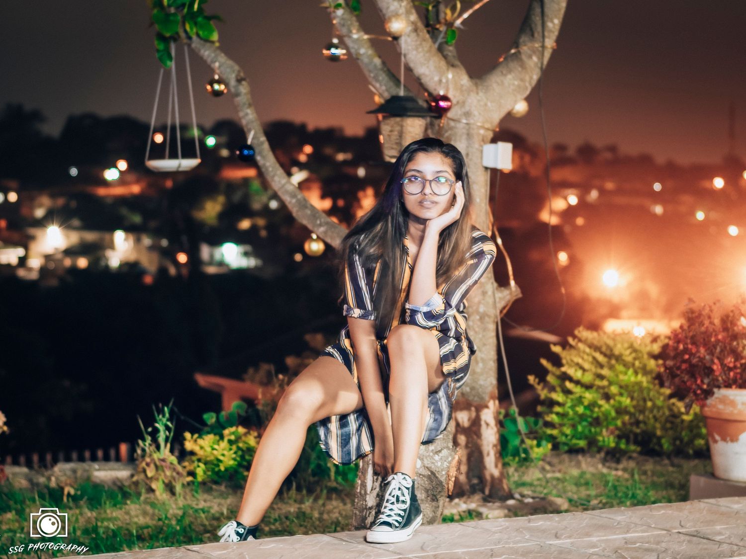 Person sitting on concrete ledge at night with city lights glowing in the background.