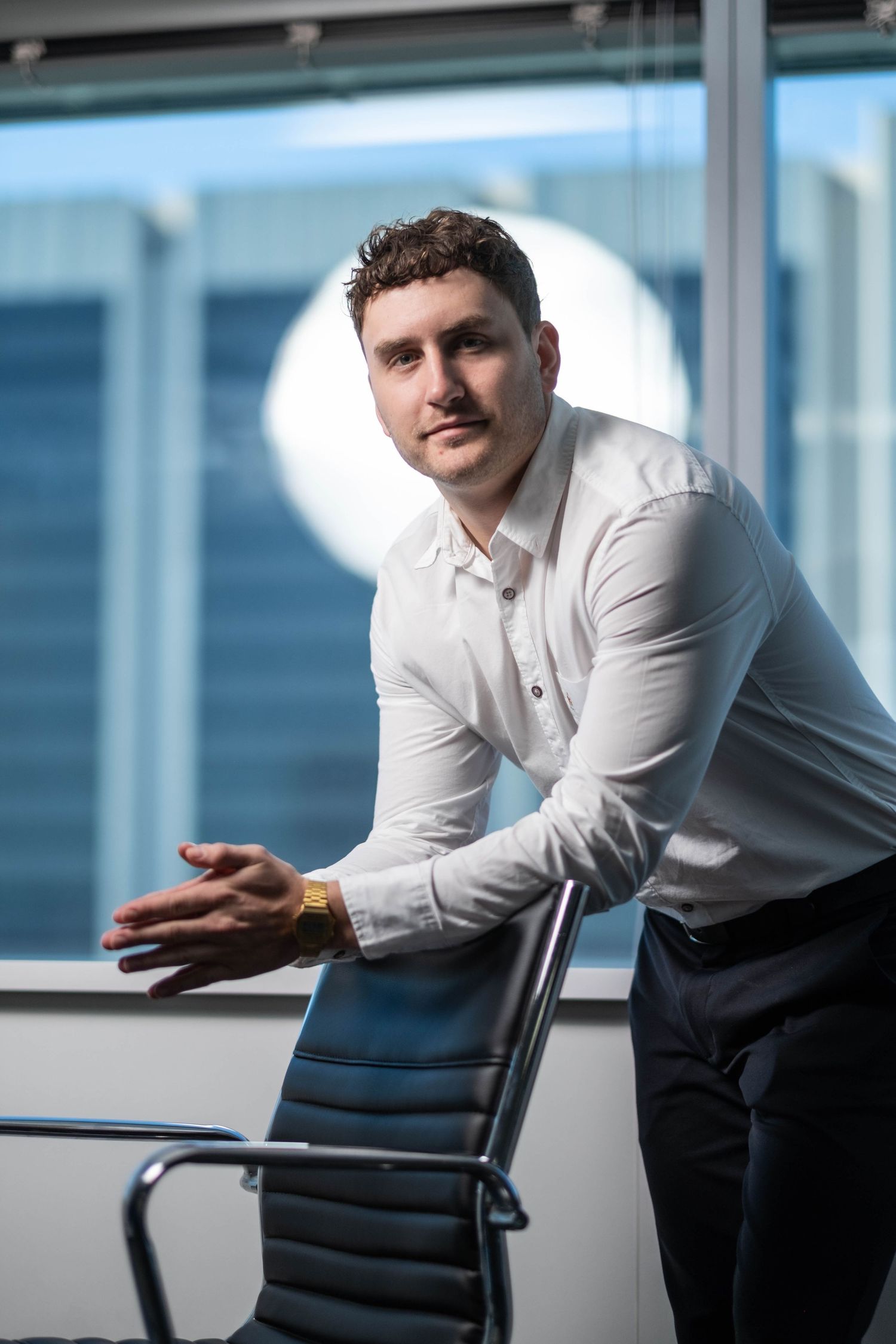 Professional in white shirt leaning on office chair in modern workspace.