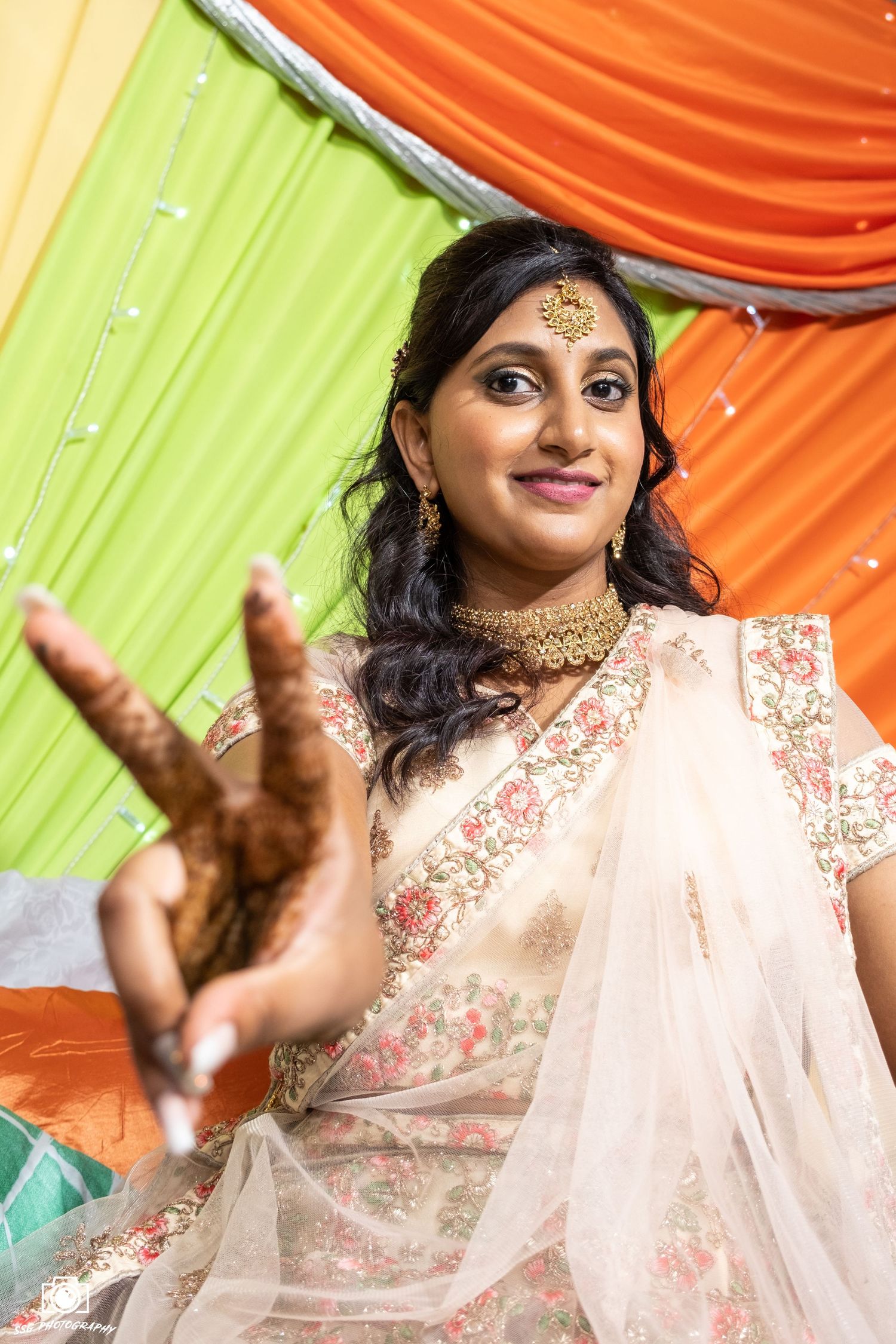 Woman in peach lehenga performs dance moves at Indian wedding celebration.