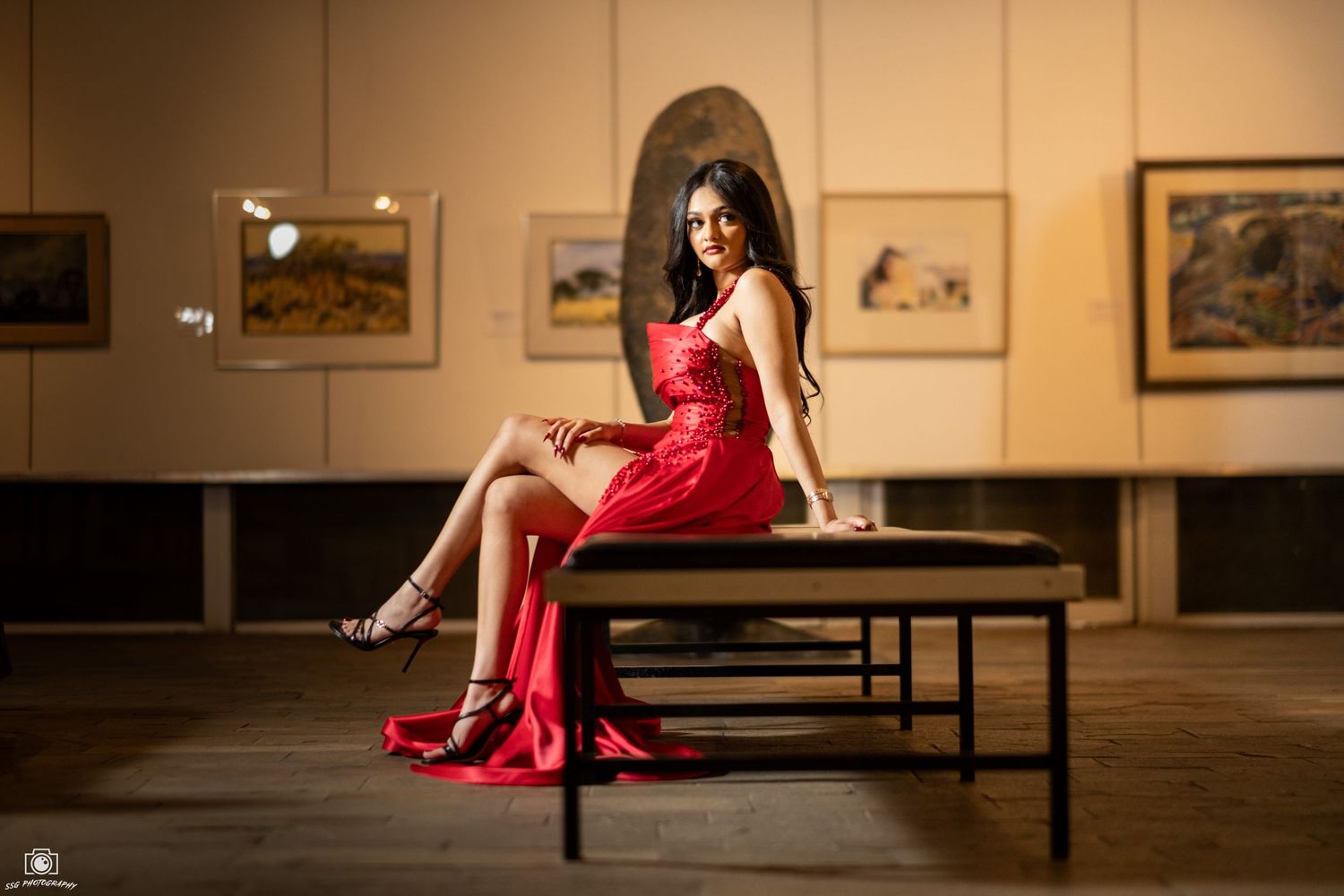 An artistic portrait in a red dress inside an art gallery with warm lighting.