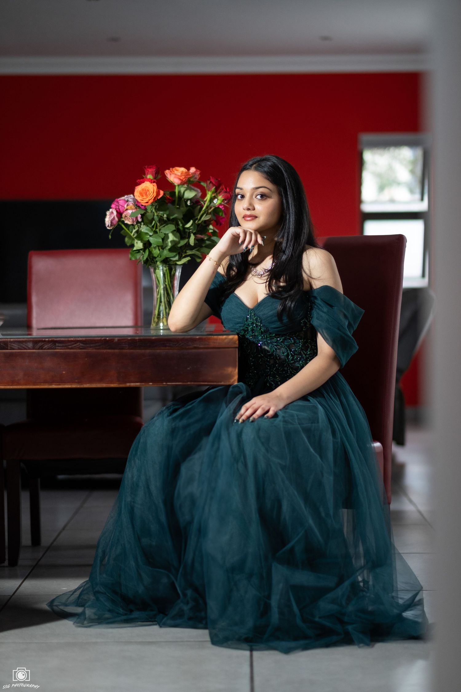Elegant portrait session with roses featuring a teal evening gown in a room with red walls.