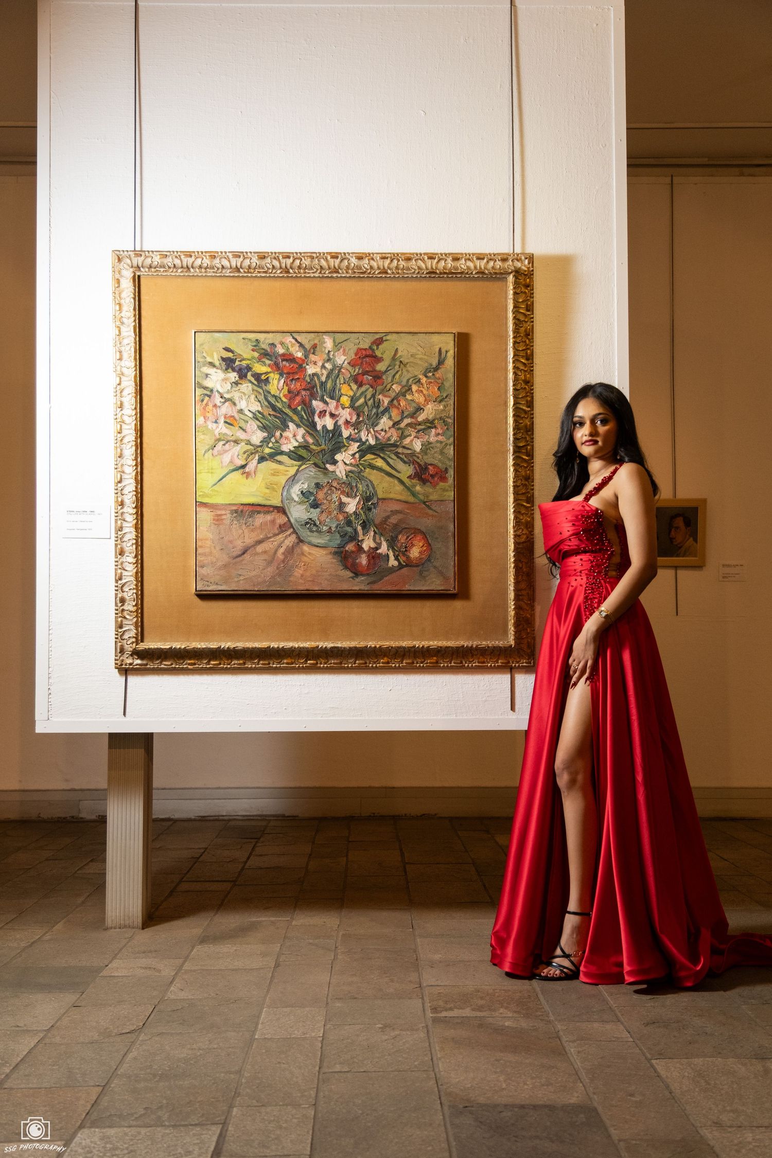 Elegant red gown photoshoot in an art gallery with framed paintings on display.