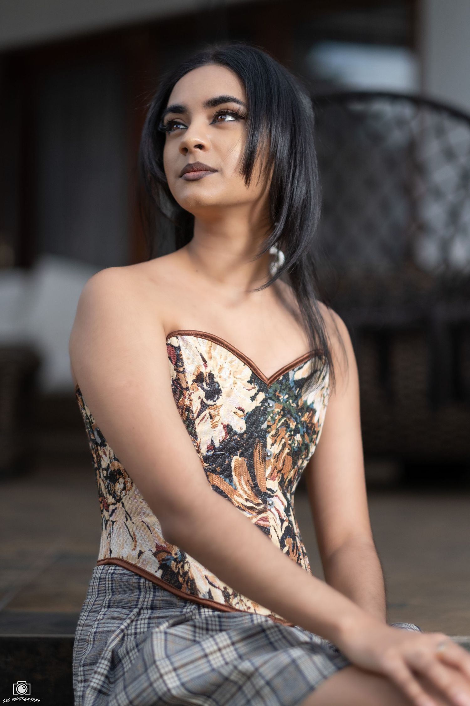 Fashion portrait featuring a patterned top and plaid skirt against rustic backdrop.