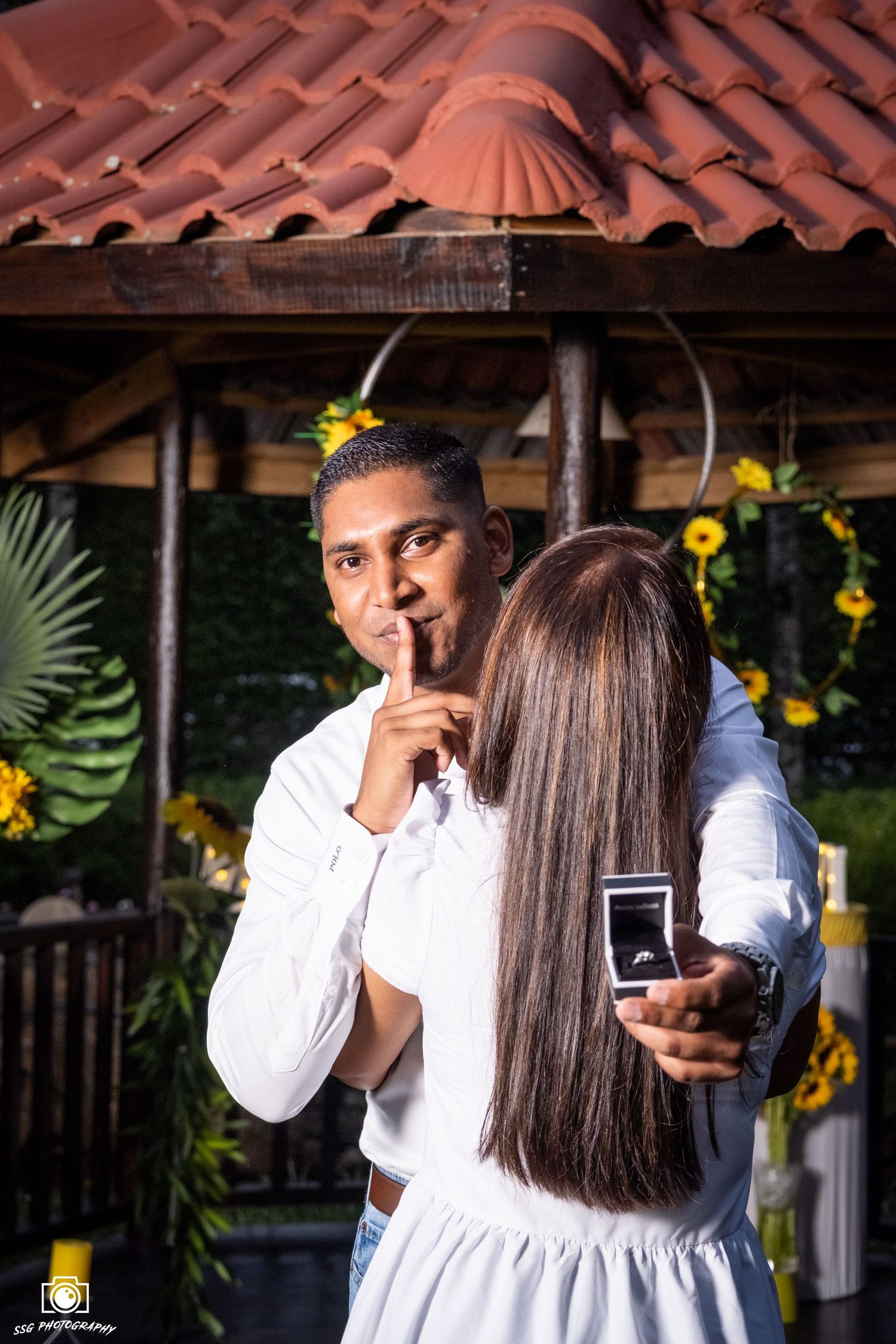 Romantic couple portrait under rustic terracotta roof with sunflowers in background.