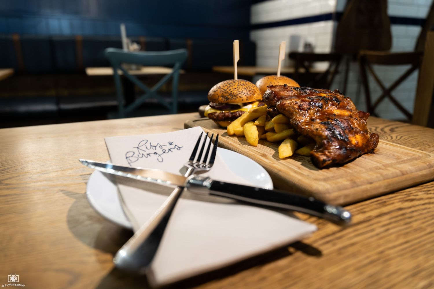 Close-up of burgers and fries served on wooden boards in restaurant setting.