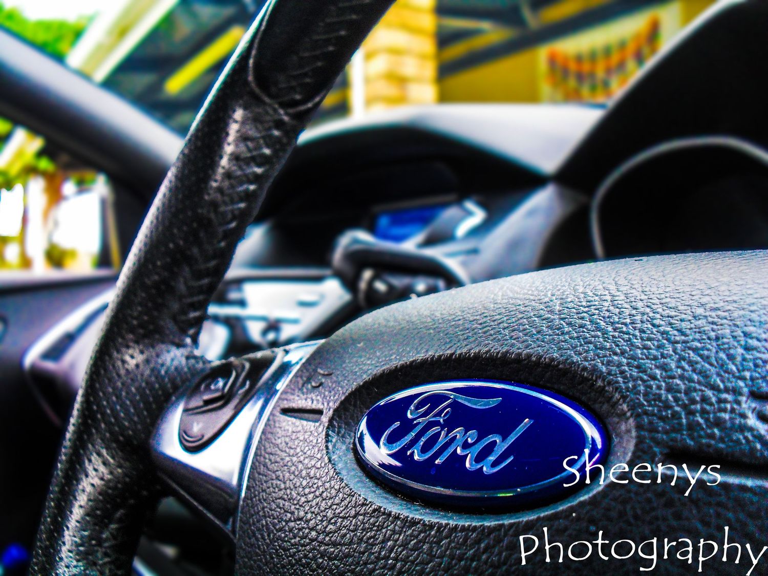 Close-up view of a Ford steering wheel with blue oval logo and textured black leather interior details.