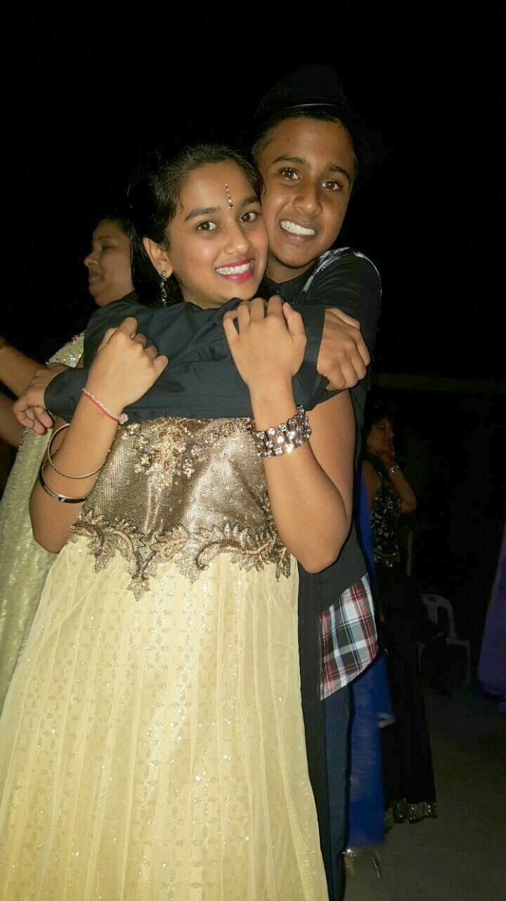 Two people embrace and smile while dancing at a nighttime event, with one wearing a sparkly cream-colored dress.