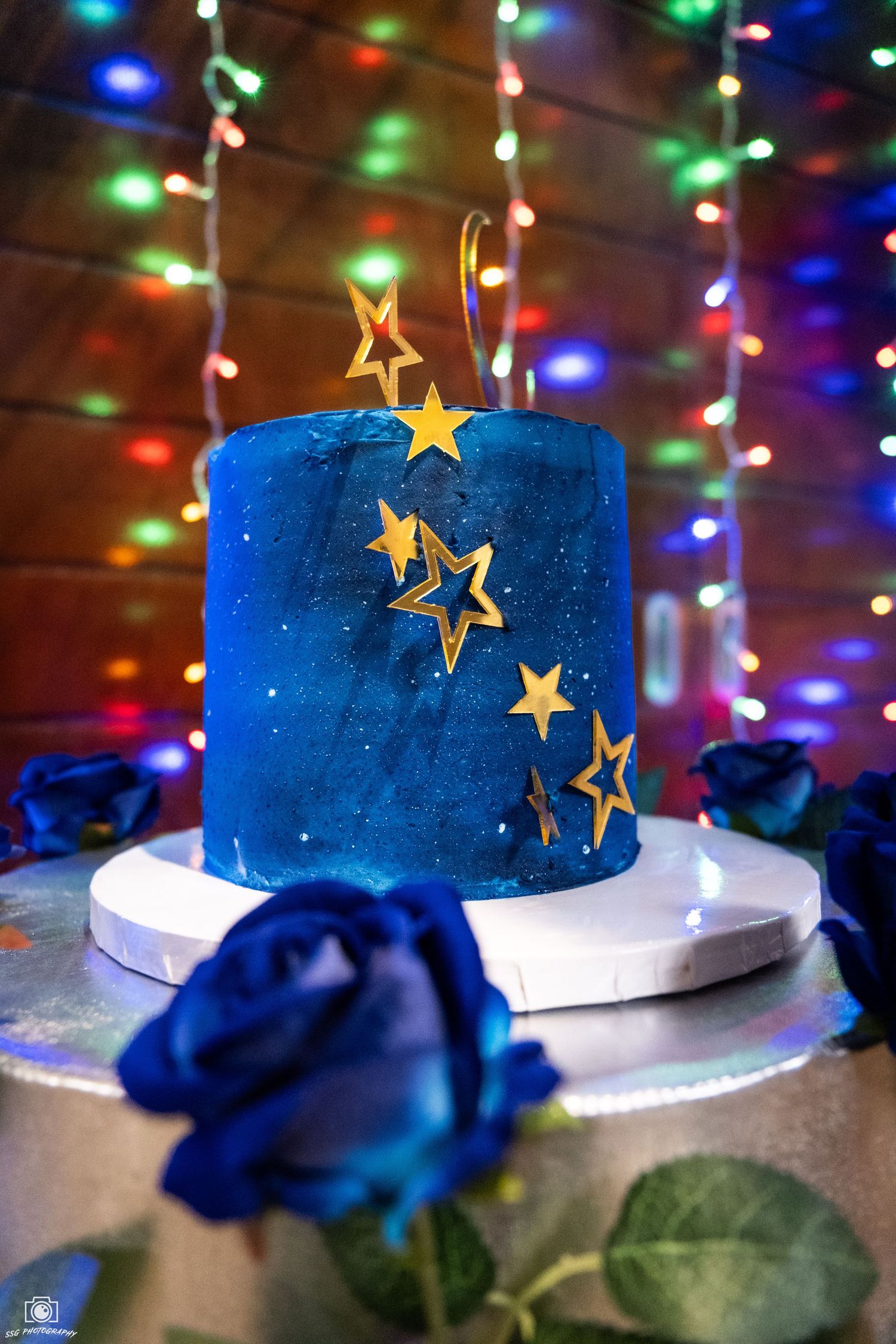 Blue cake decorated with golden stars and colorful lights in the background.