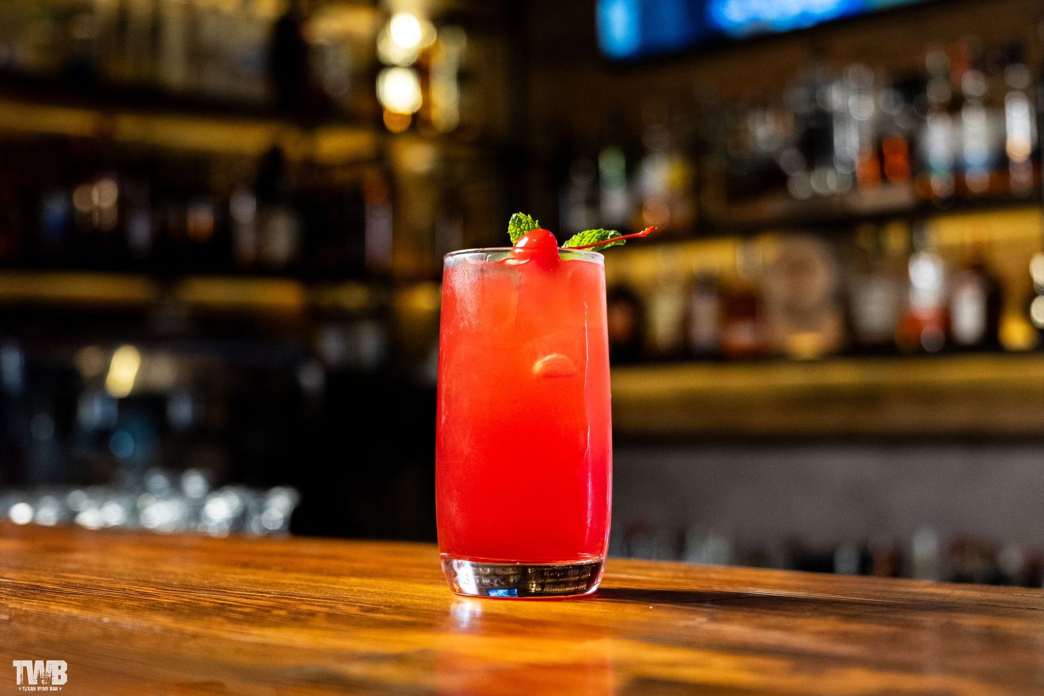 Vibrant red cocktails with fresh garnishes lined up on a wooden bar counter.