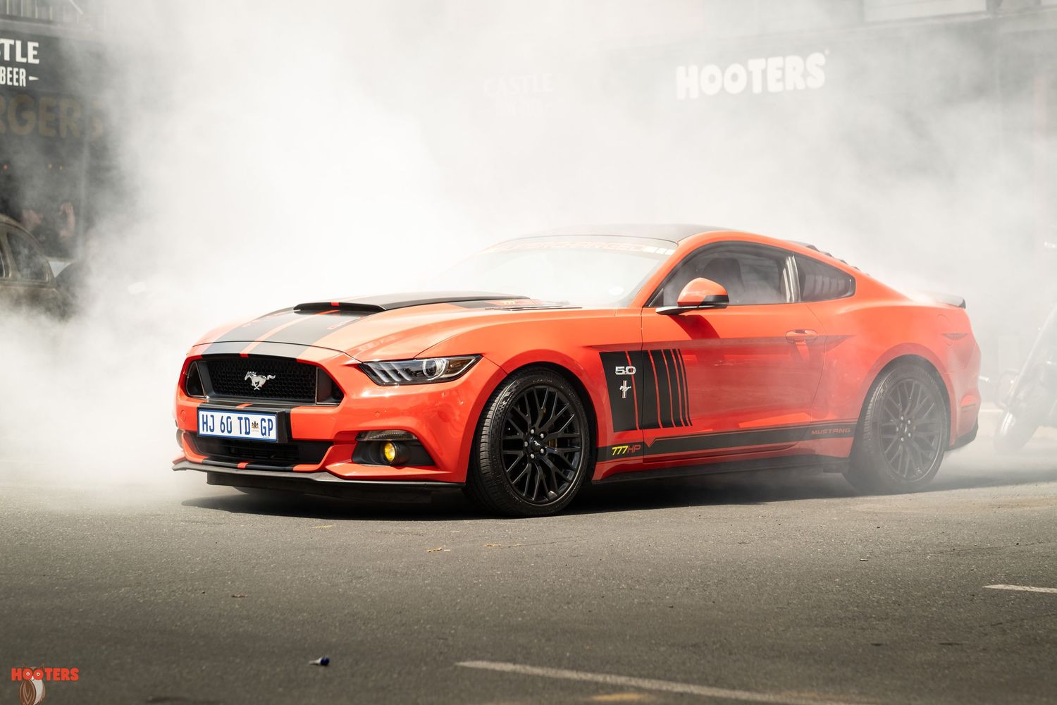 Orange sports cars creating smoke while performing burnouts on asphalt.