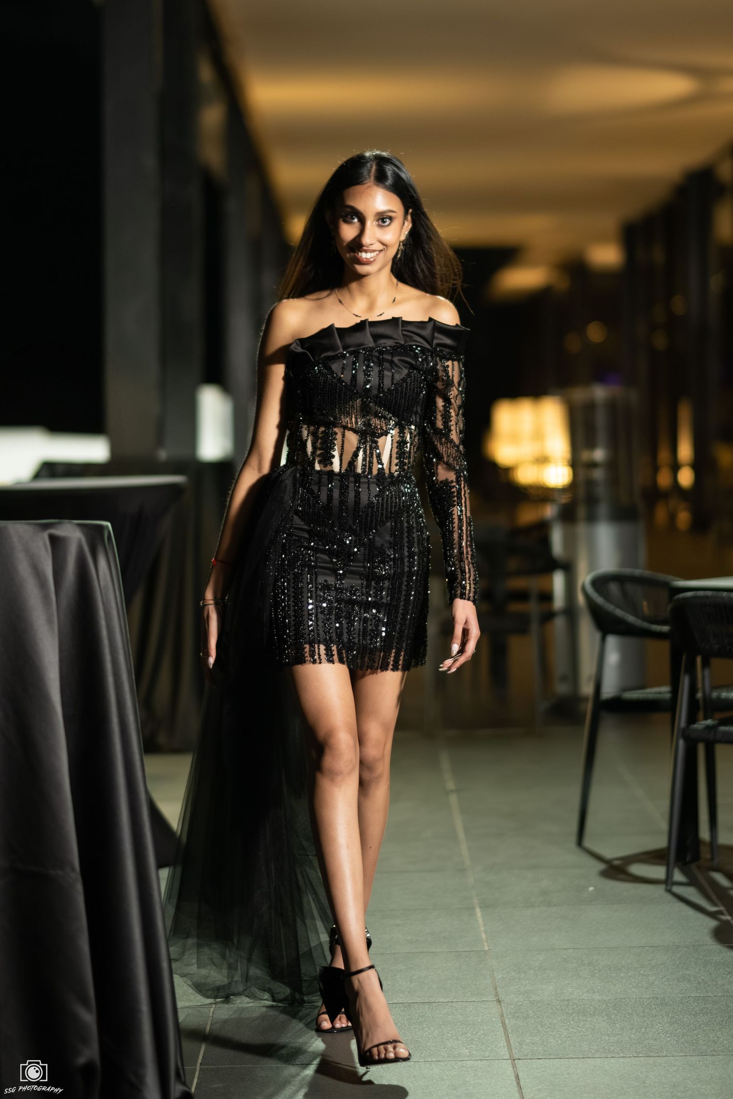Fashion photography in a modern indoor setting with black furniture and ambient lighting.
