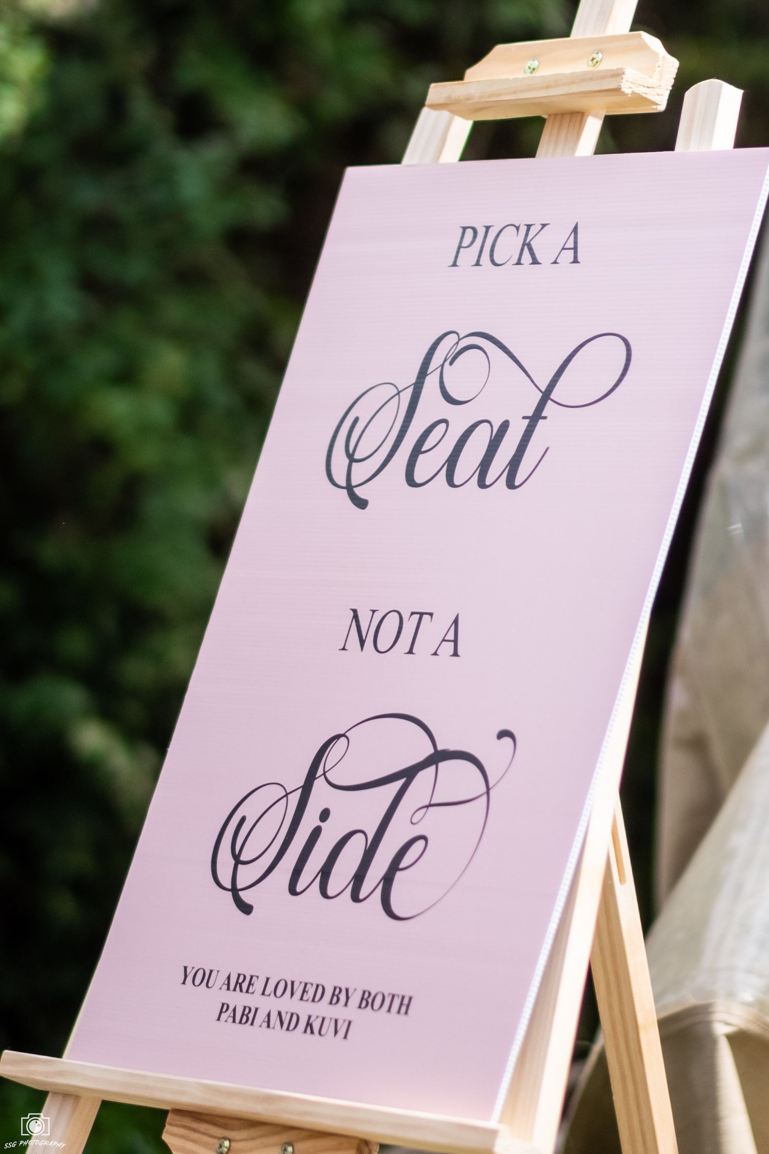 Wedding signage displays in pink and white on wooden easels against a garden backdrop.