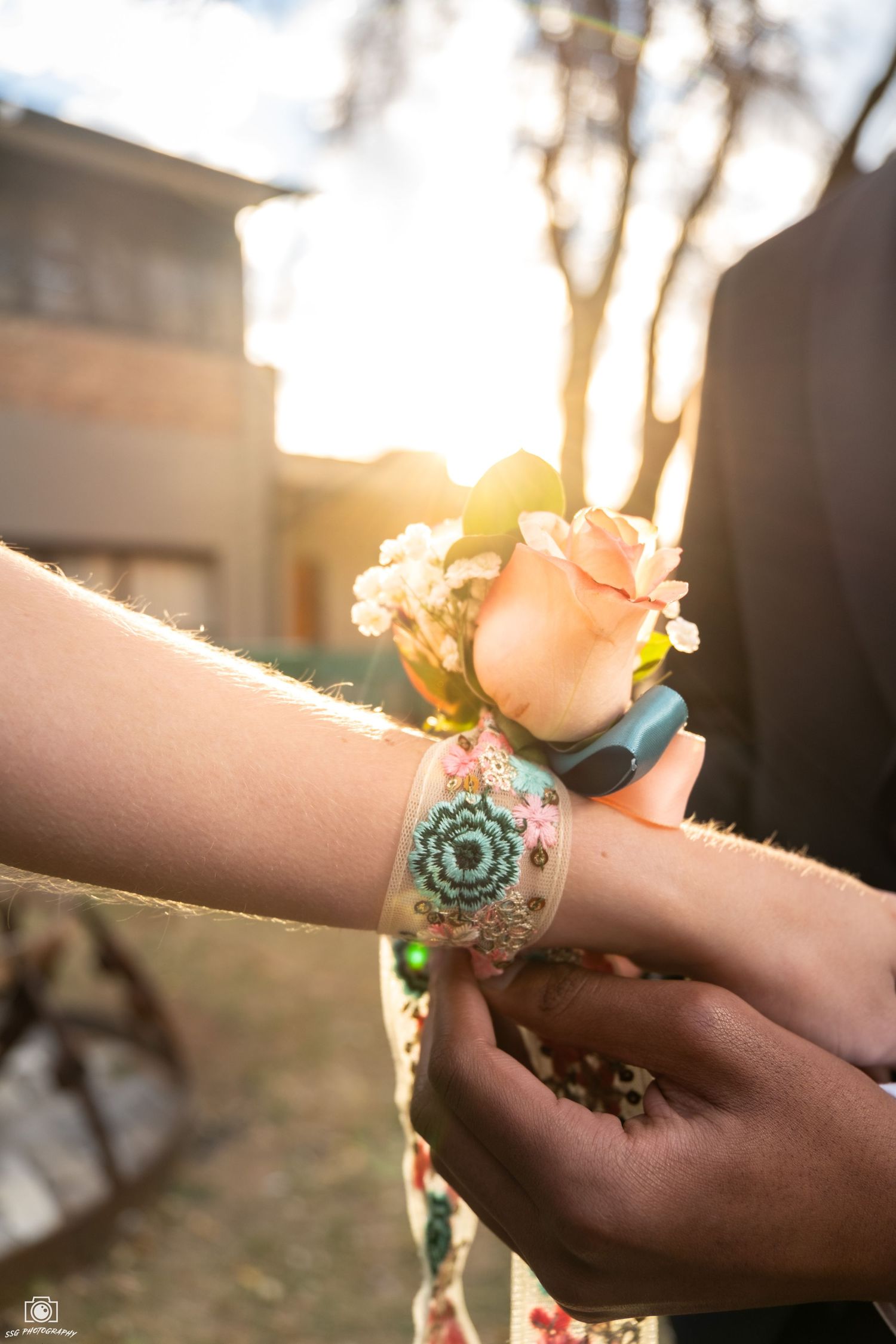 Close-up of hands with bracelets reaching toward golden sunlight during sunset.