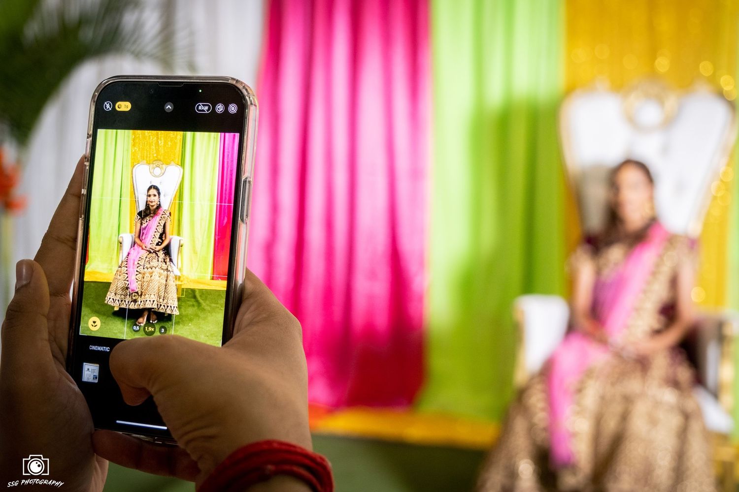 Colorful backdrop with pink and yellow drapes while someone takes photos on a smartphone.