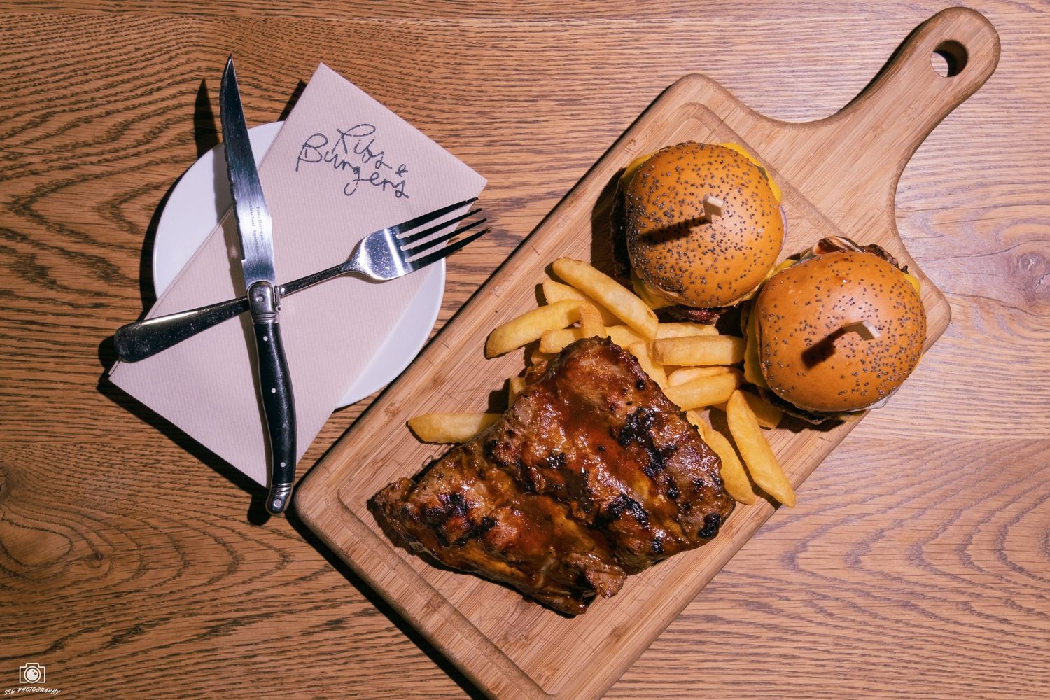 Burgers and ribs plated on wooden serving boards with branded paper liners.