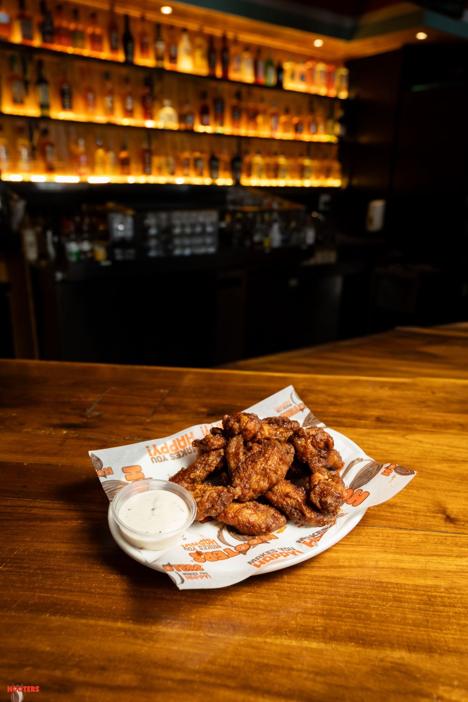 Crispy chicken wings with ranch dipping sauce served on branded paper in a bar setting.