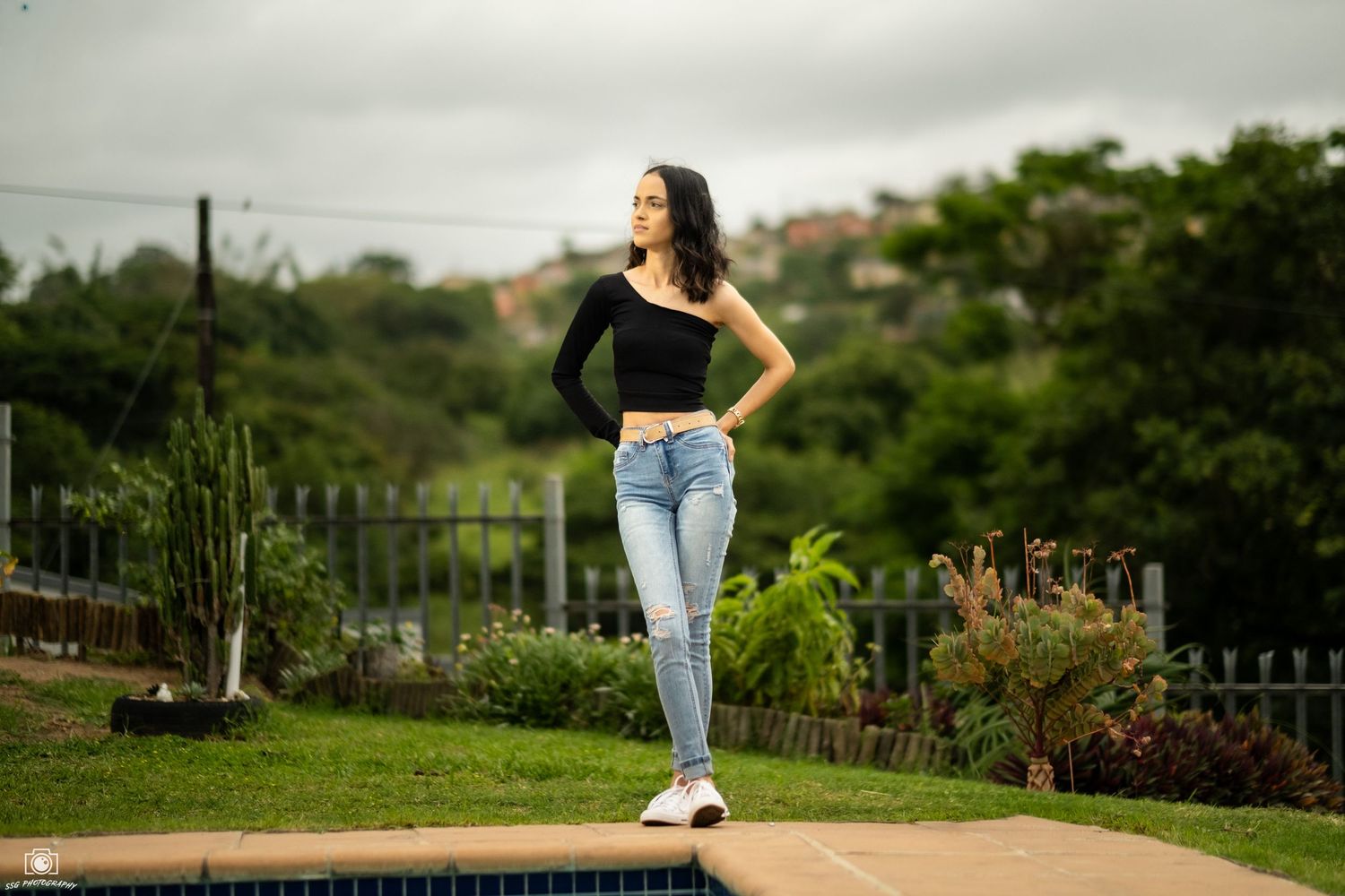 A casual outdoor photoshoot featuring someone in ripped jeans and a black sweater against a green natural background.