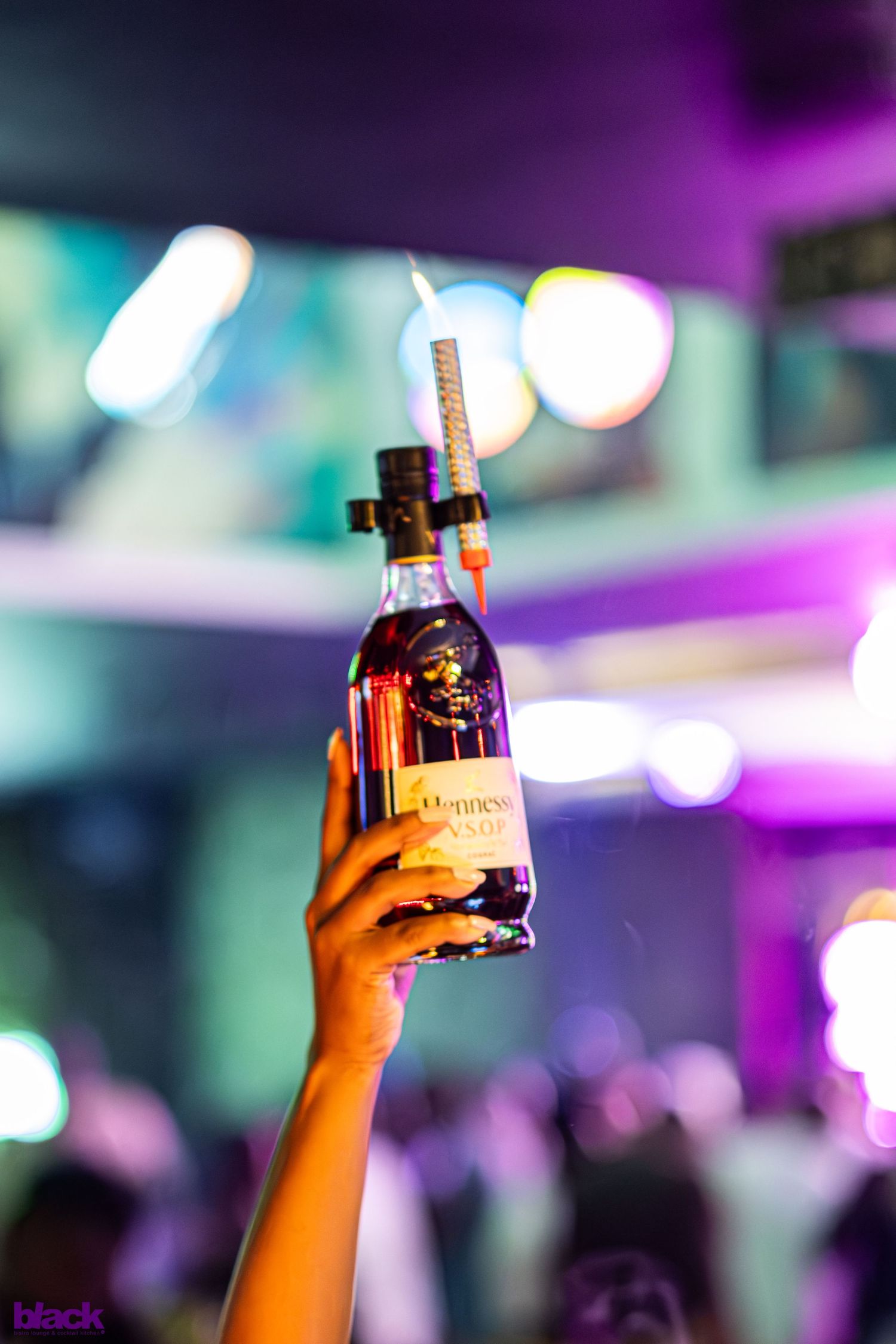 Hands holding up bottles against colorful nightclub lighting.