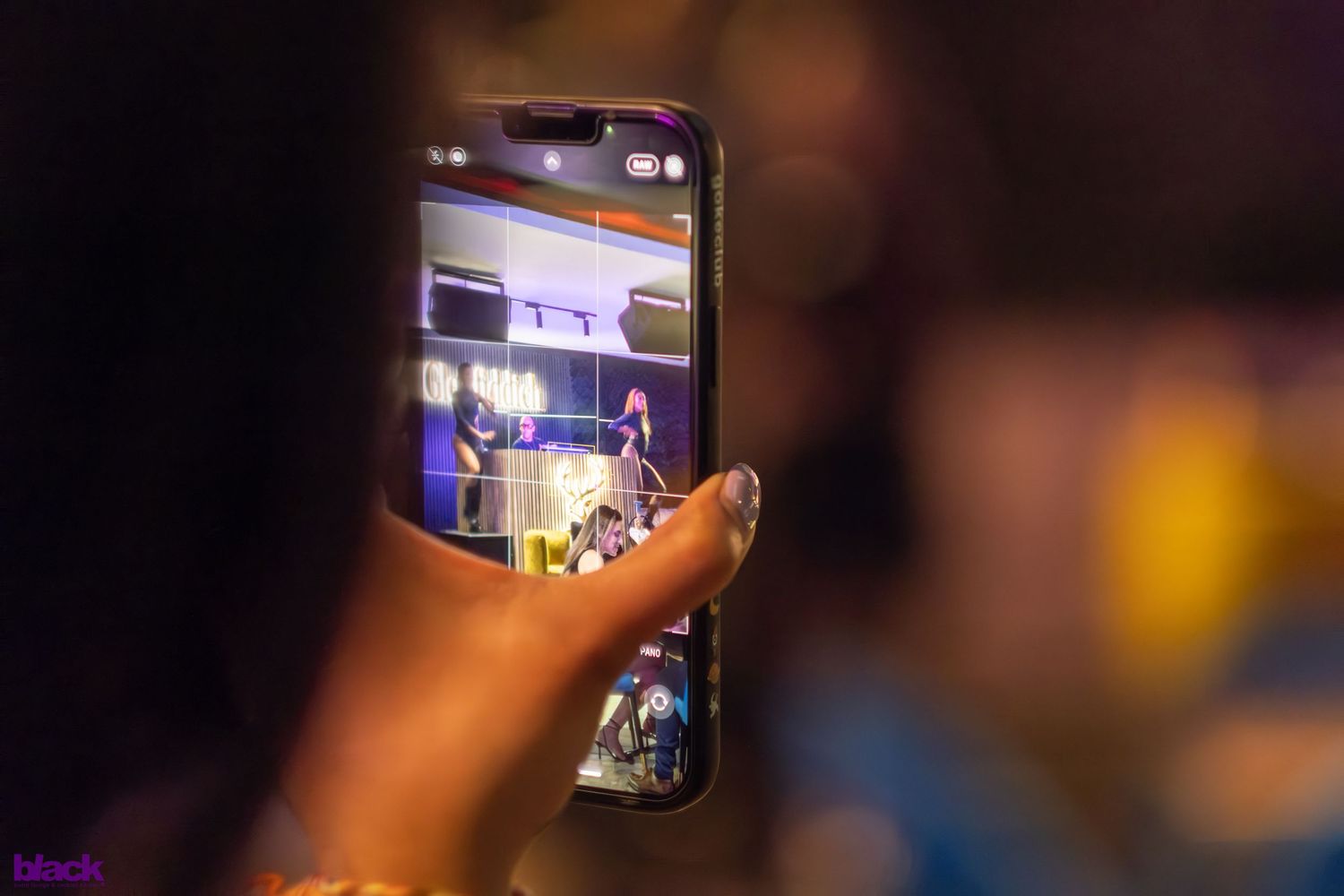 Hand holding phone captures performance on stage through camera screen.