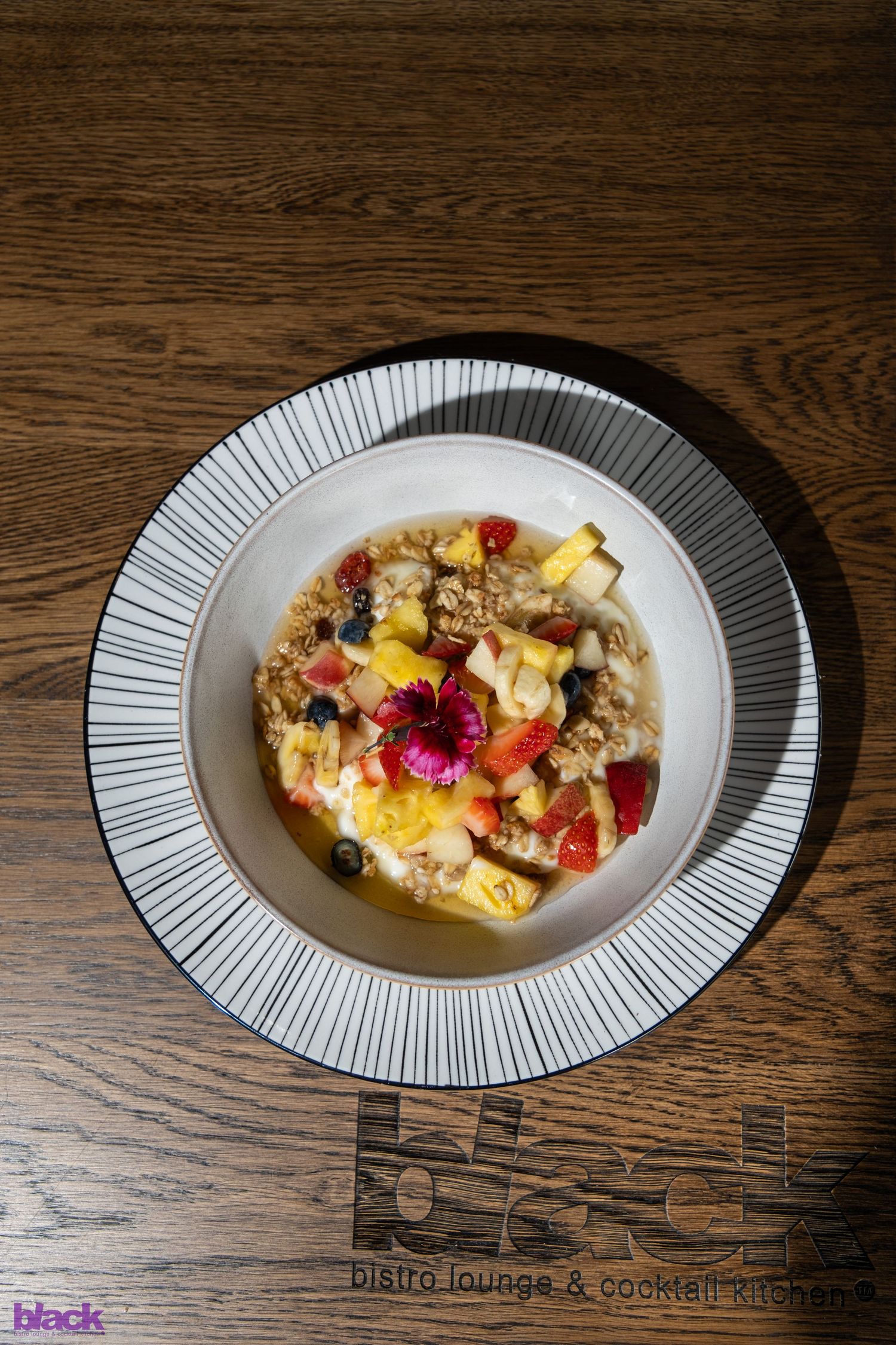 Colorful breakfast bowl with fresh fruits and granola served on a modern striped plate.