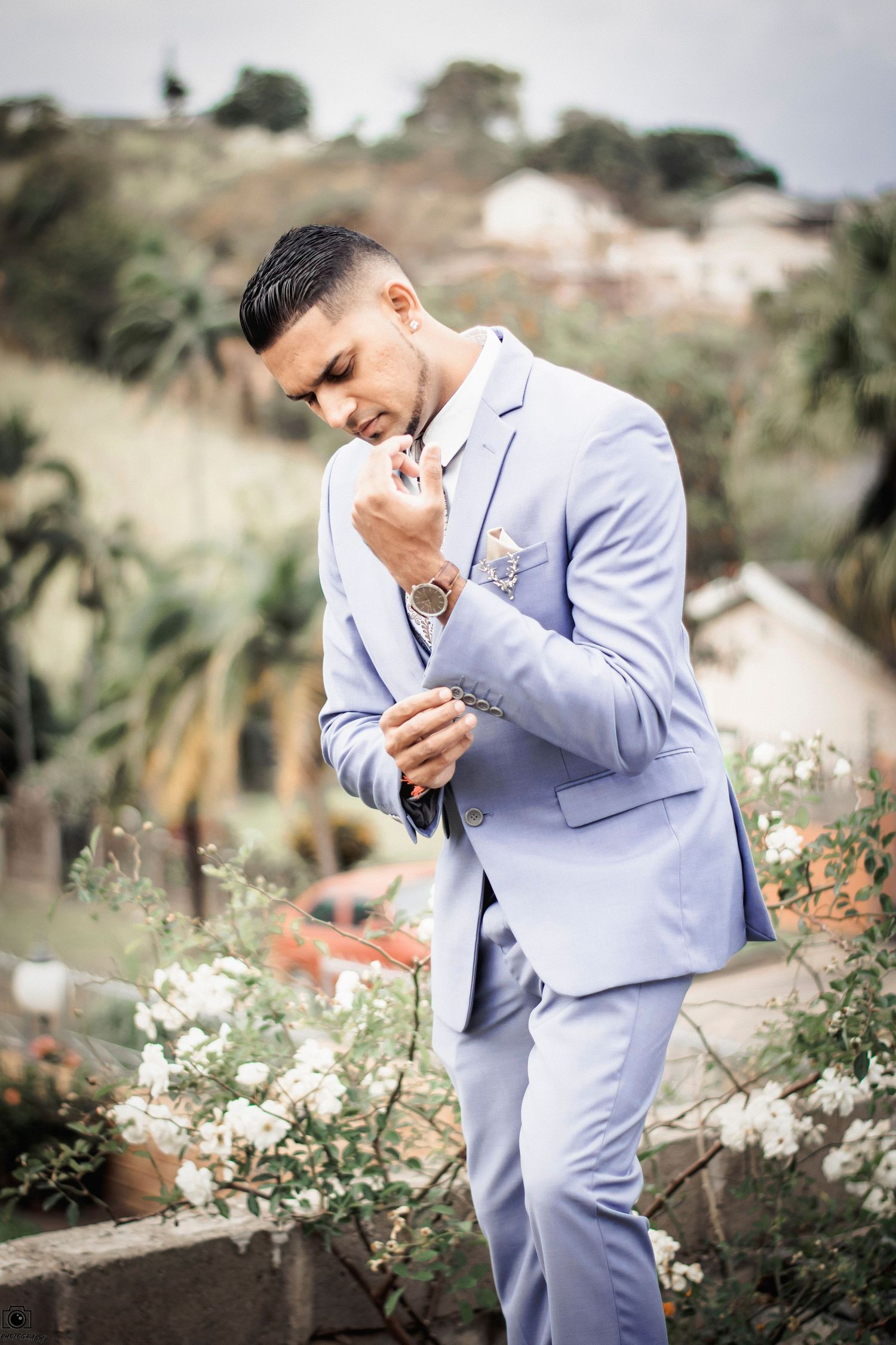Stylish groom in powder blue suit posing in garden setting with white flowers.