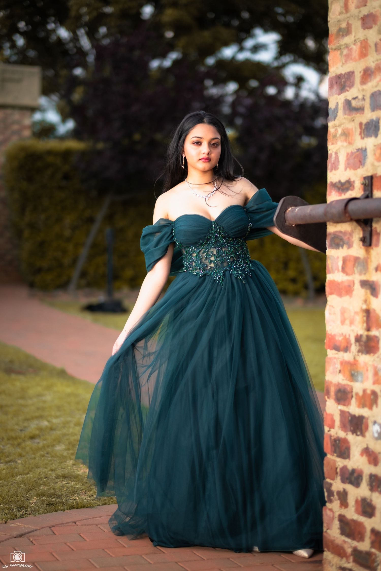 Portrait series featuring emerald green ball gown against brick architectural backdrop.