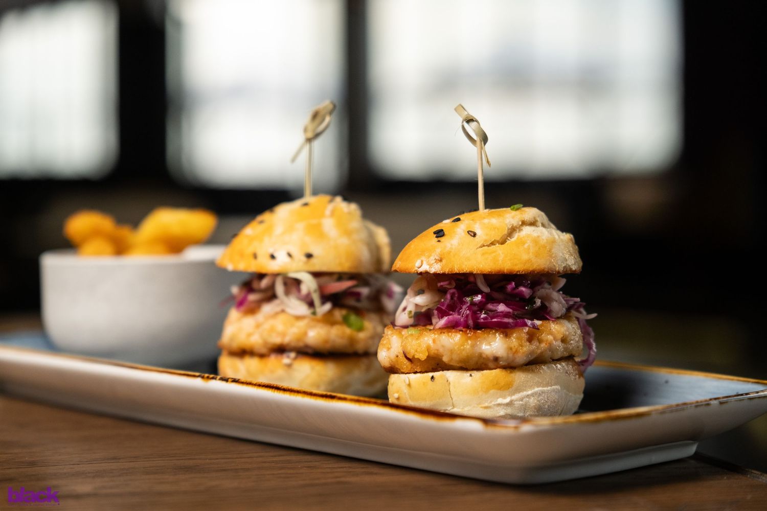 Two gourmet sliders with red cabbage slaw served on white rectangular plate.