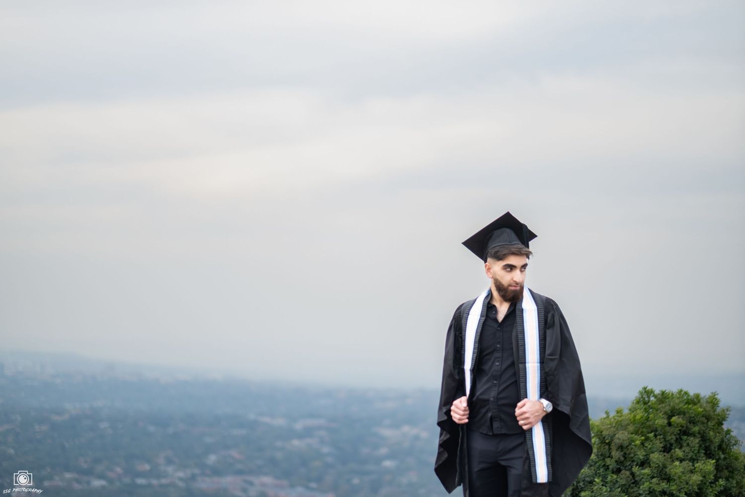 Graduation photoshoot on a hilltop with scenic mountain views in the background.