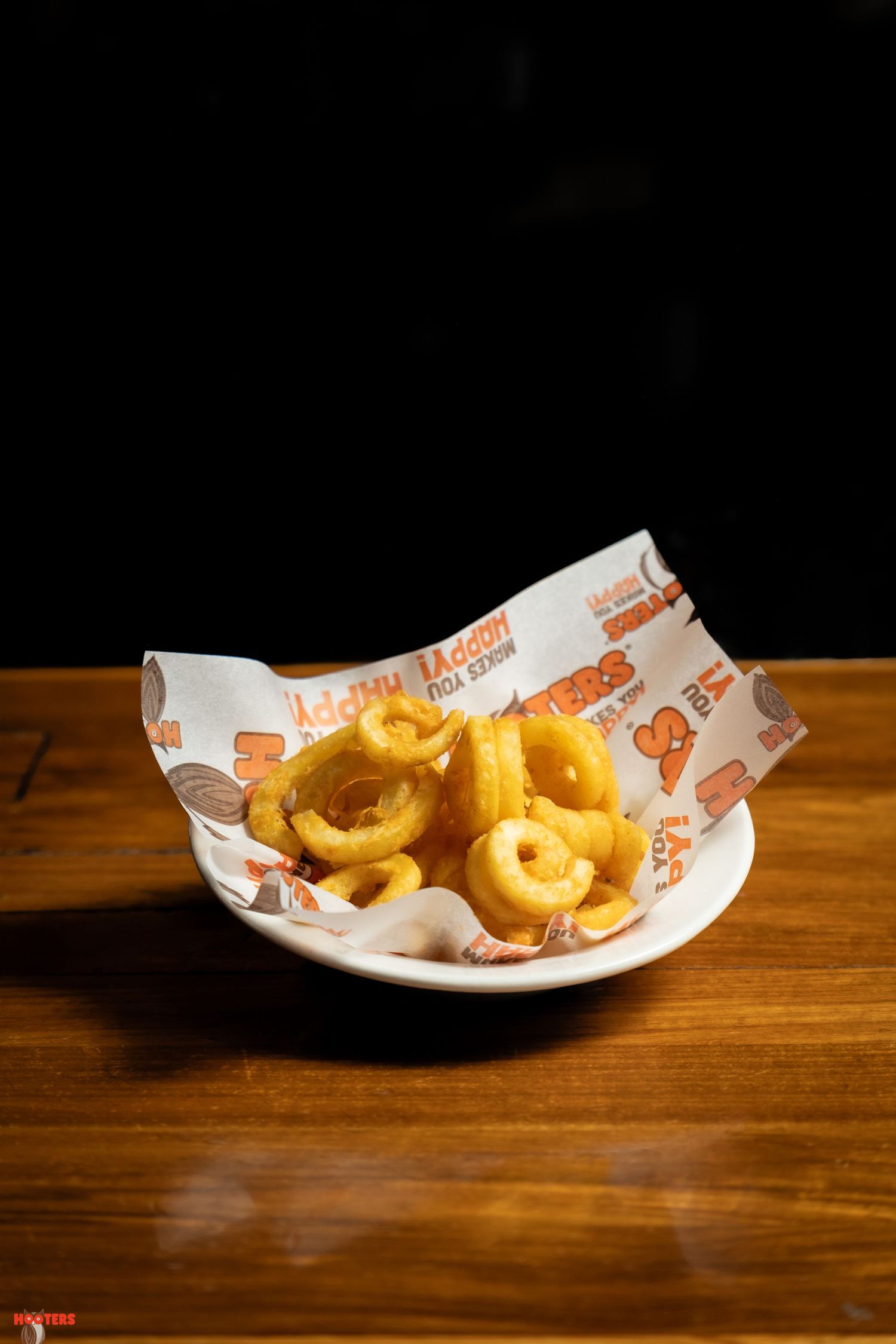 Crispy curly fries served in branded paper wrapper on white plate with dramatic lighting.
