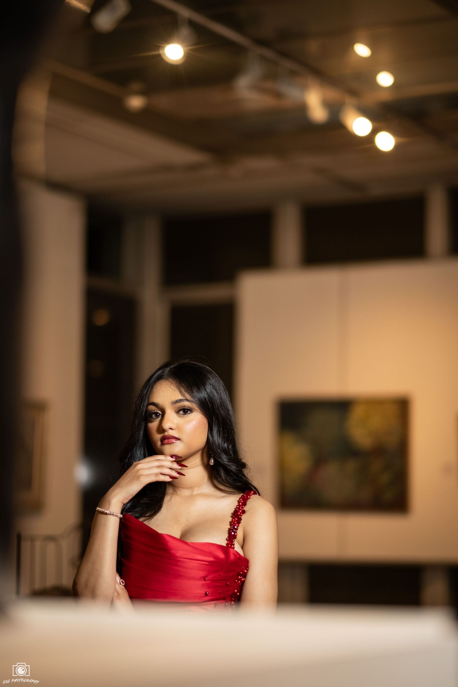 Dramatic portrait session in red dress against gallery walls with moody lighting.