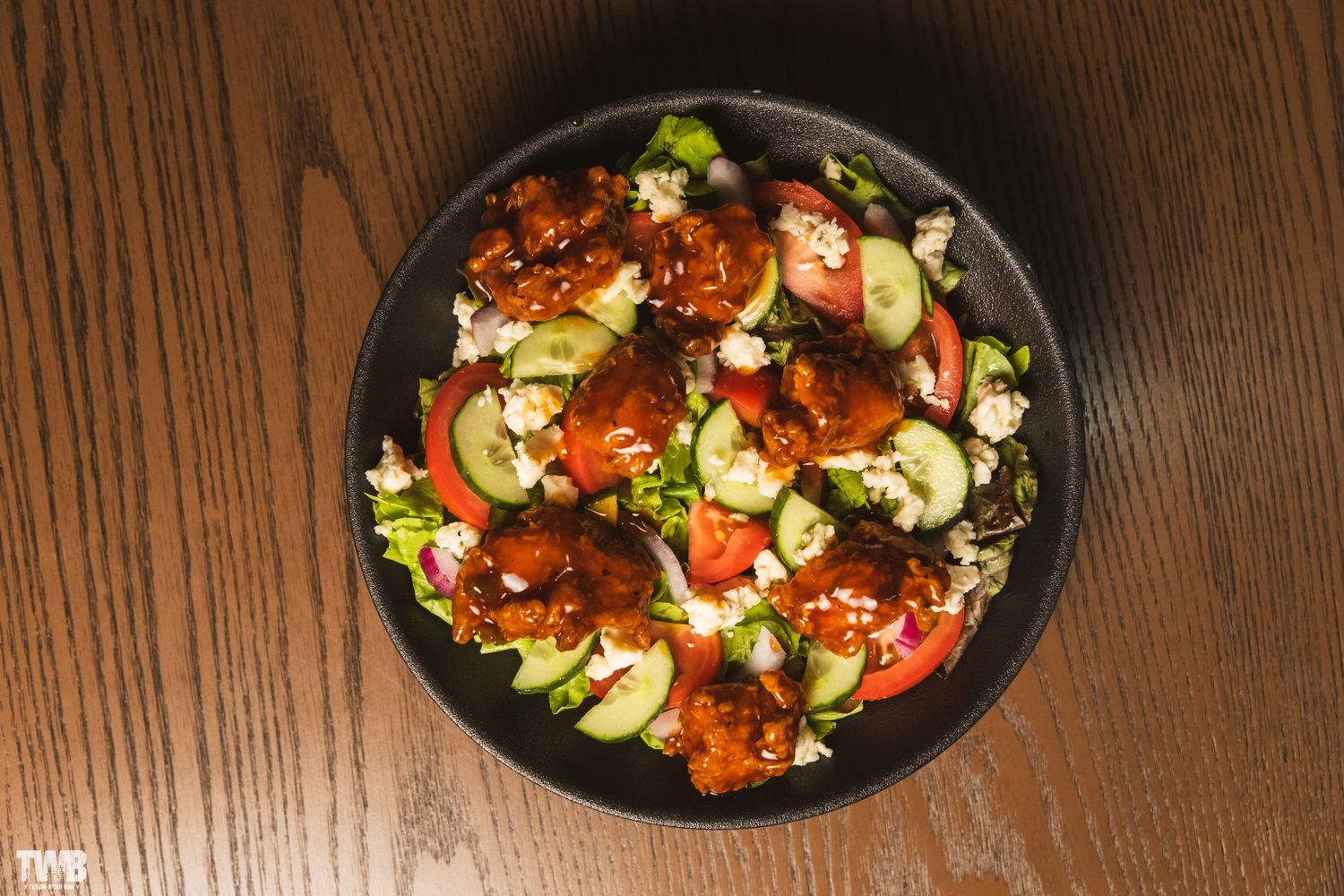 Fresh salad with tomatoes and greens served on black plates in restaurant setting.