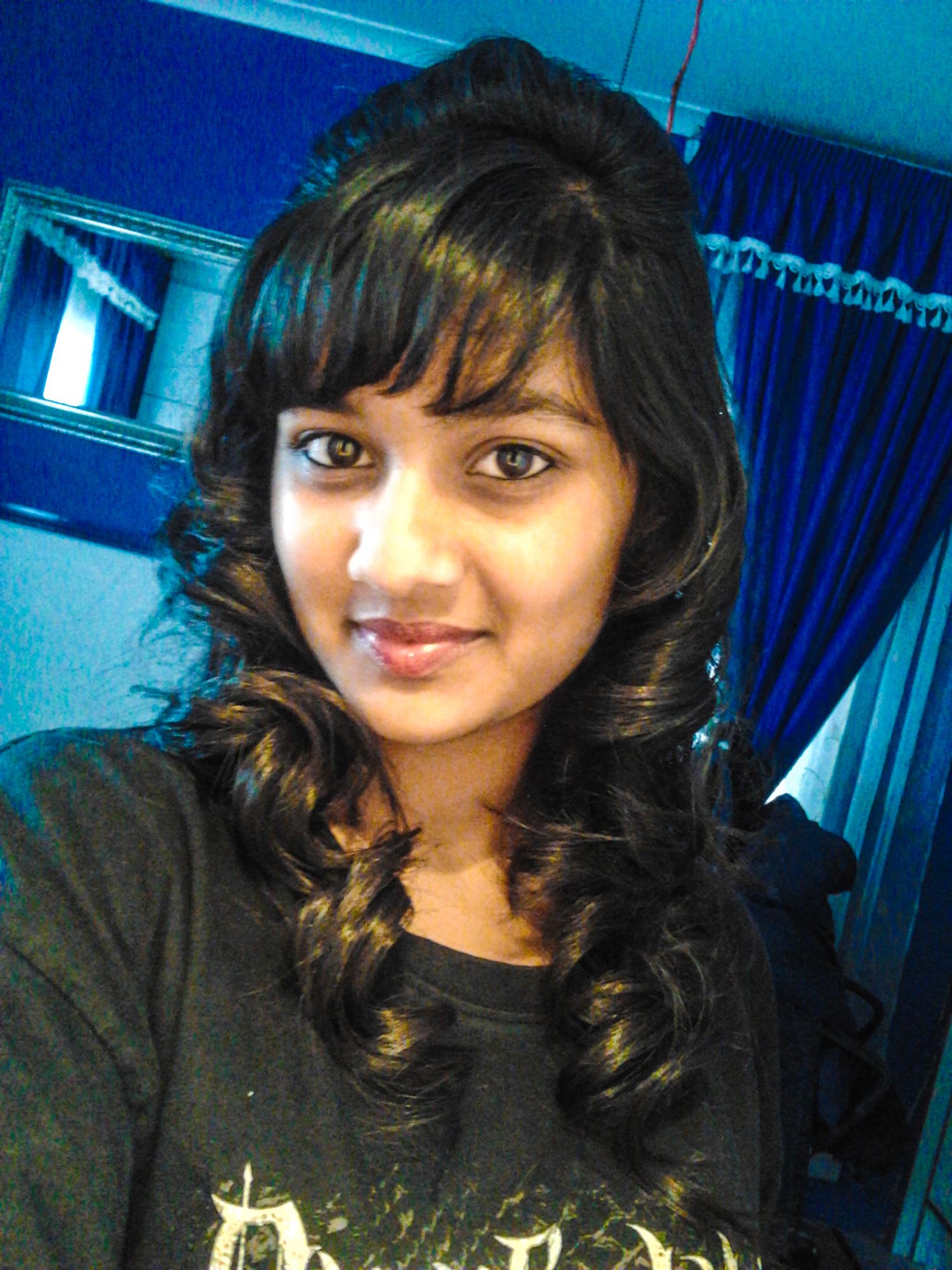A person with dark wavy hair wearing a black top poses against a blue-tinted background in a selfie-style photo series.