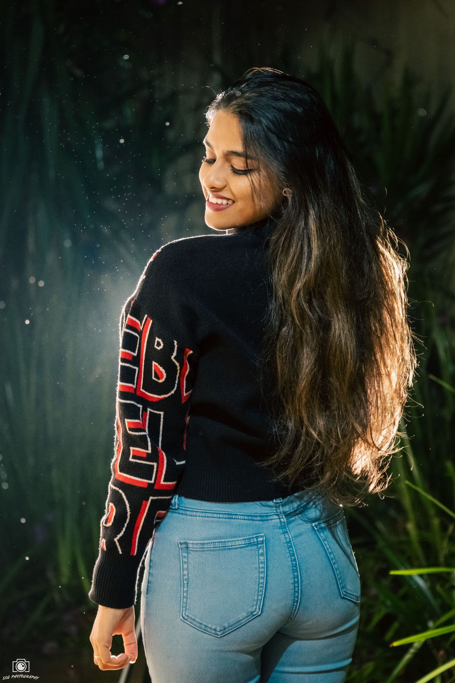 Artistic back view portrait showing a black sweater with red text and light denim jeans.