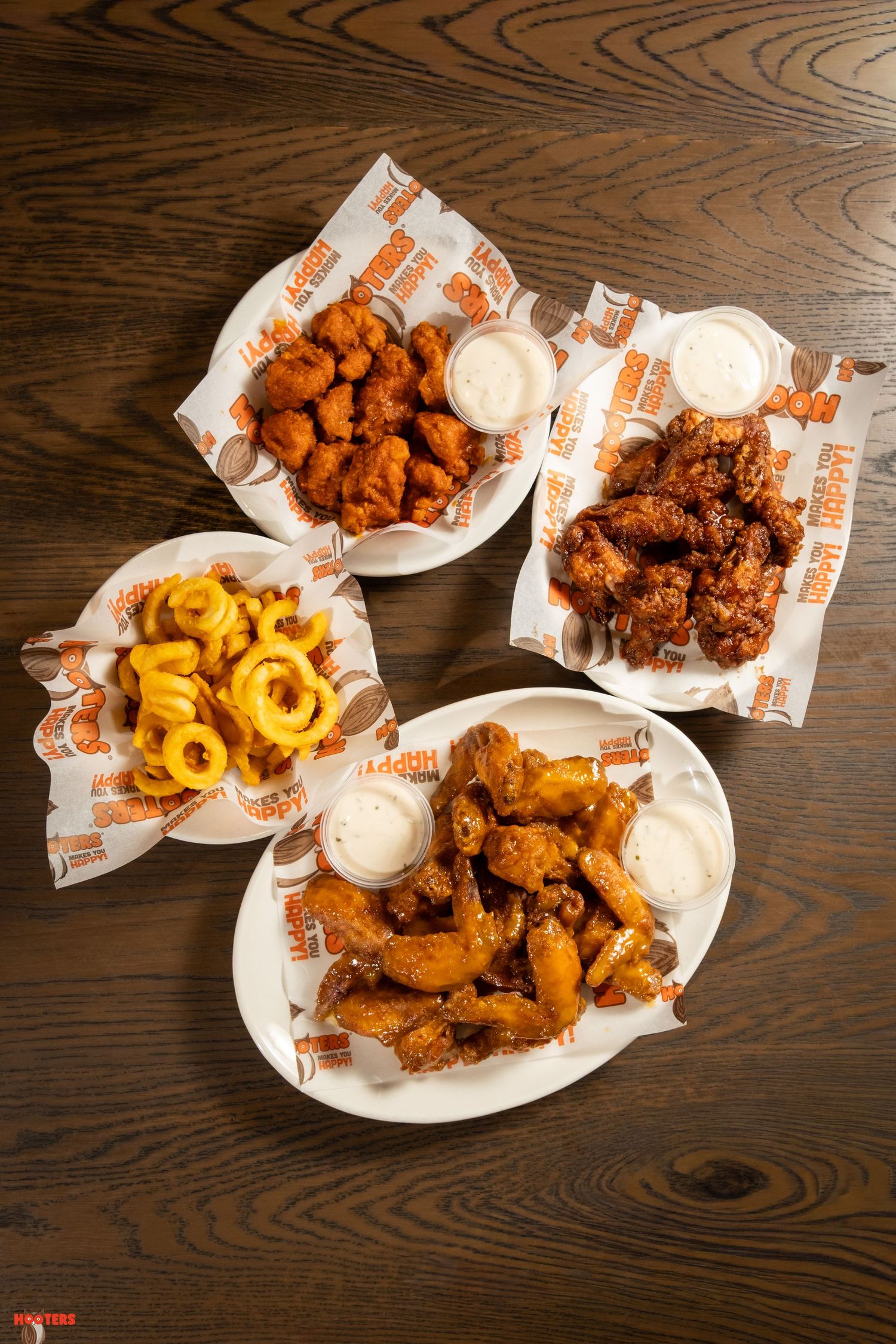 Overhead view of various chicken wings and curly fries with dipping sauces served on white plates.