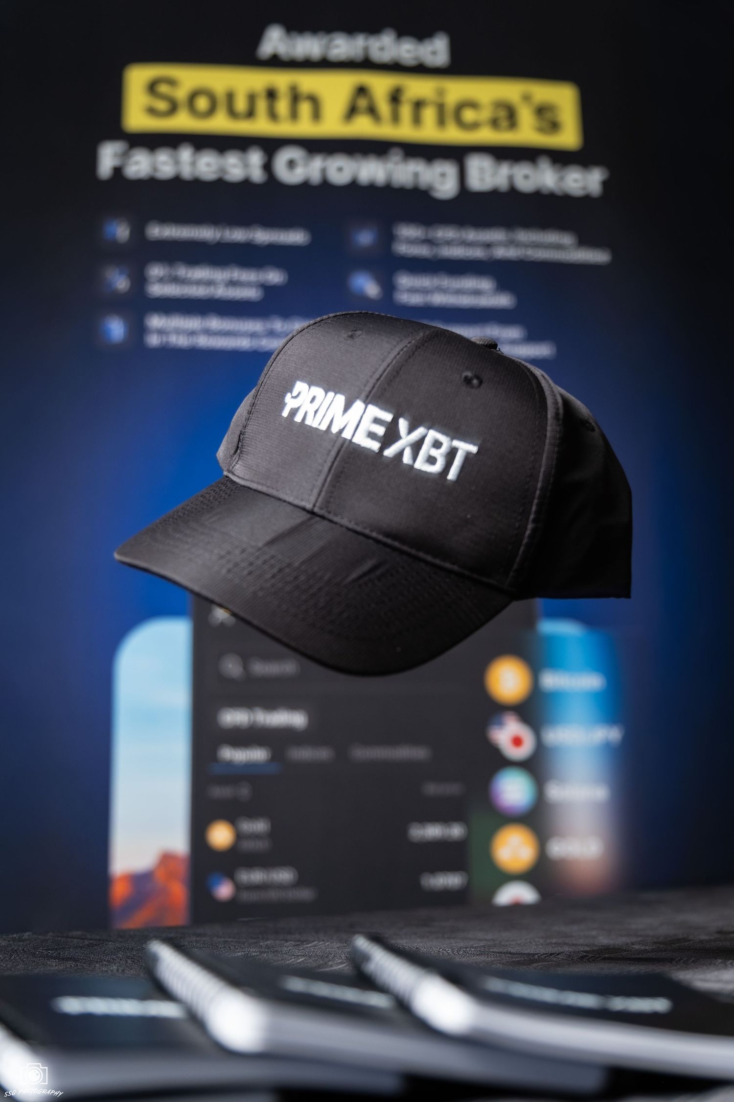Black PRIME XBT branded baseball cap displayed against financial trading screens and statistics.