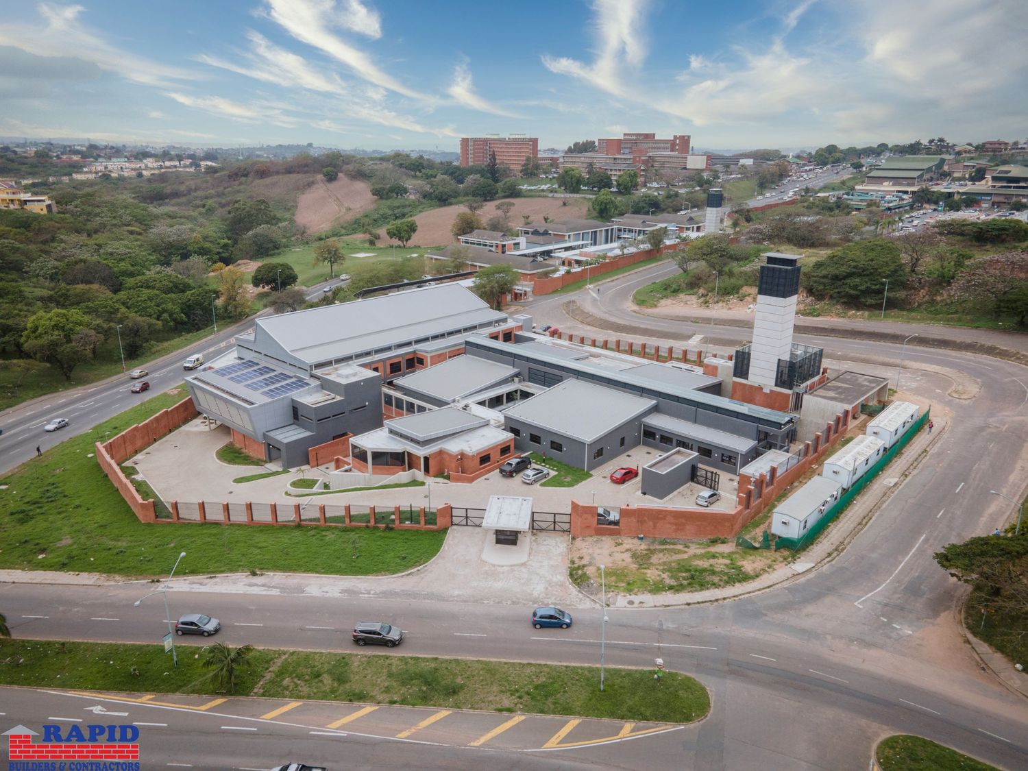 Aerial view of commercial buildings and parking lots under blue sky with white clouds.