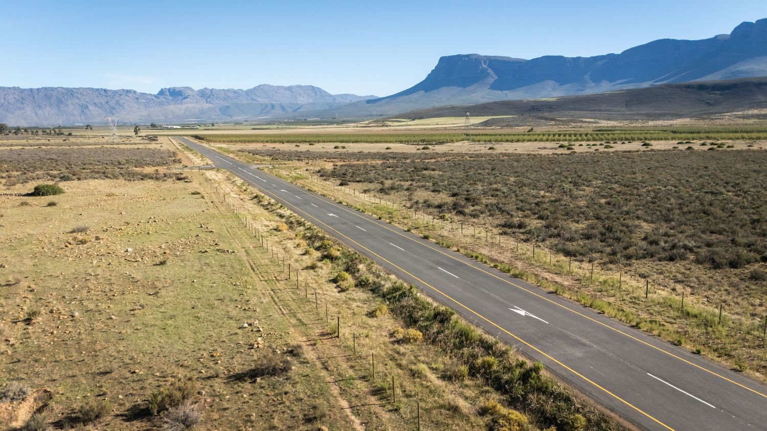 Long empty highway stretching through arid desert landscape with mountains in background.