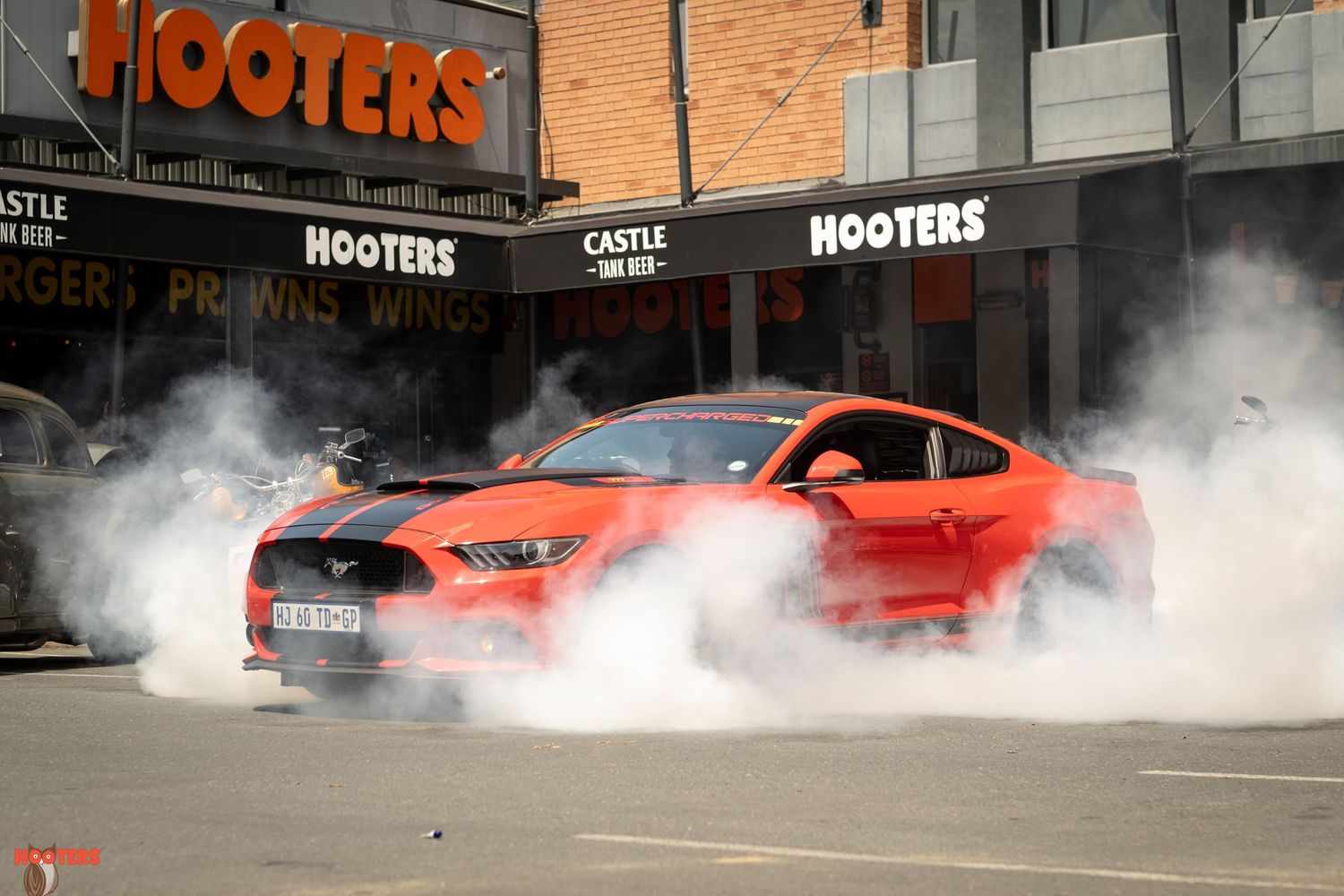 Orange Mustang performing dramatic burnouts in front of a Hooters restaurant.