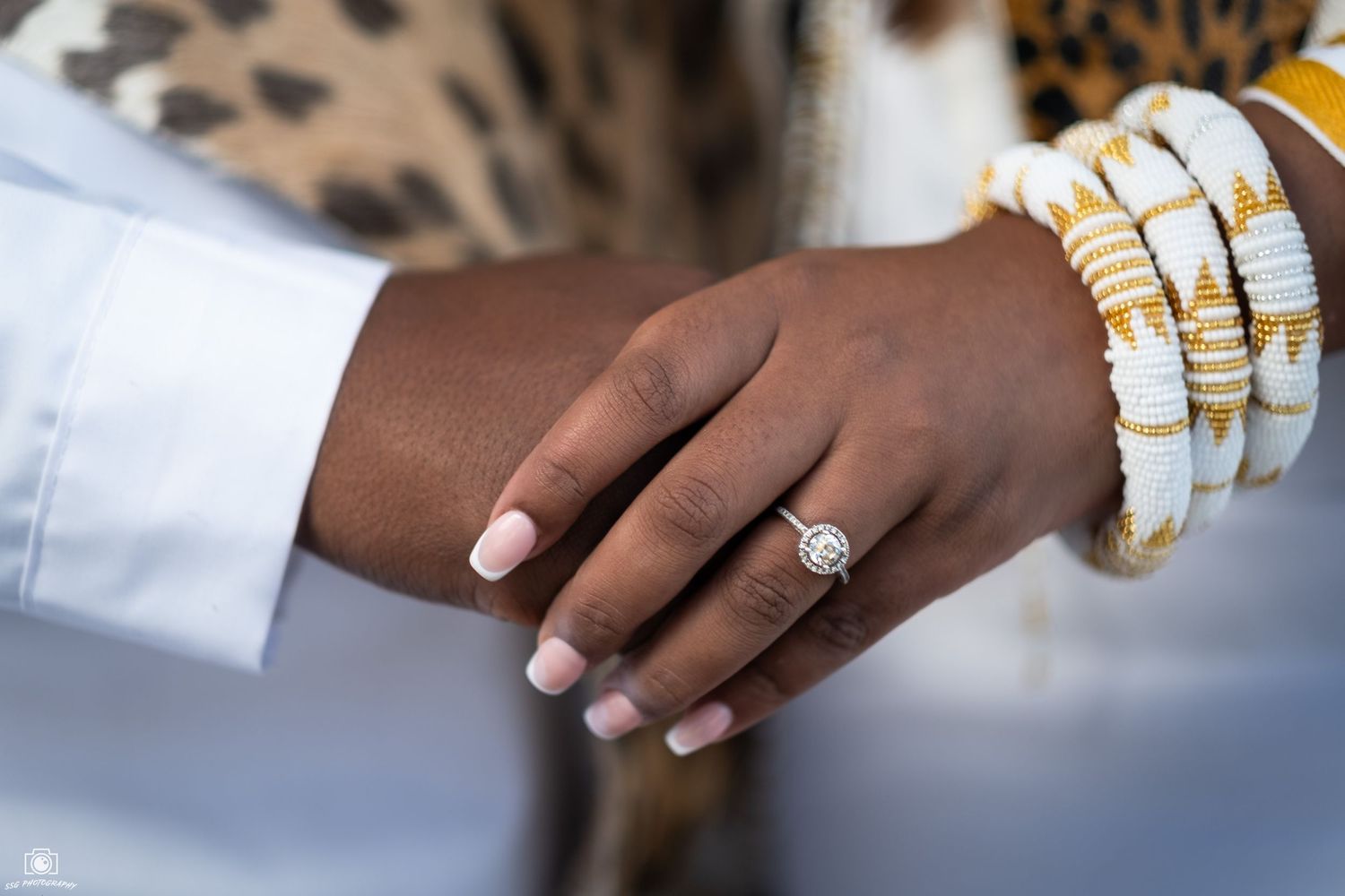 Close-up of hands wearing multiple gold rings and white nail polish.