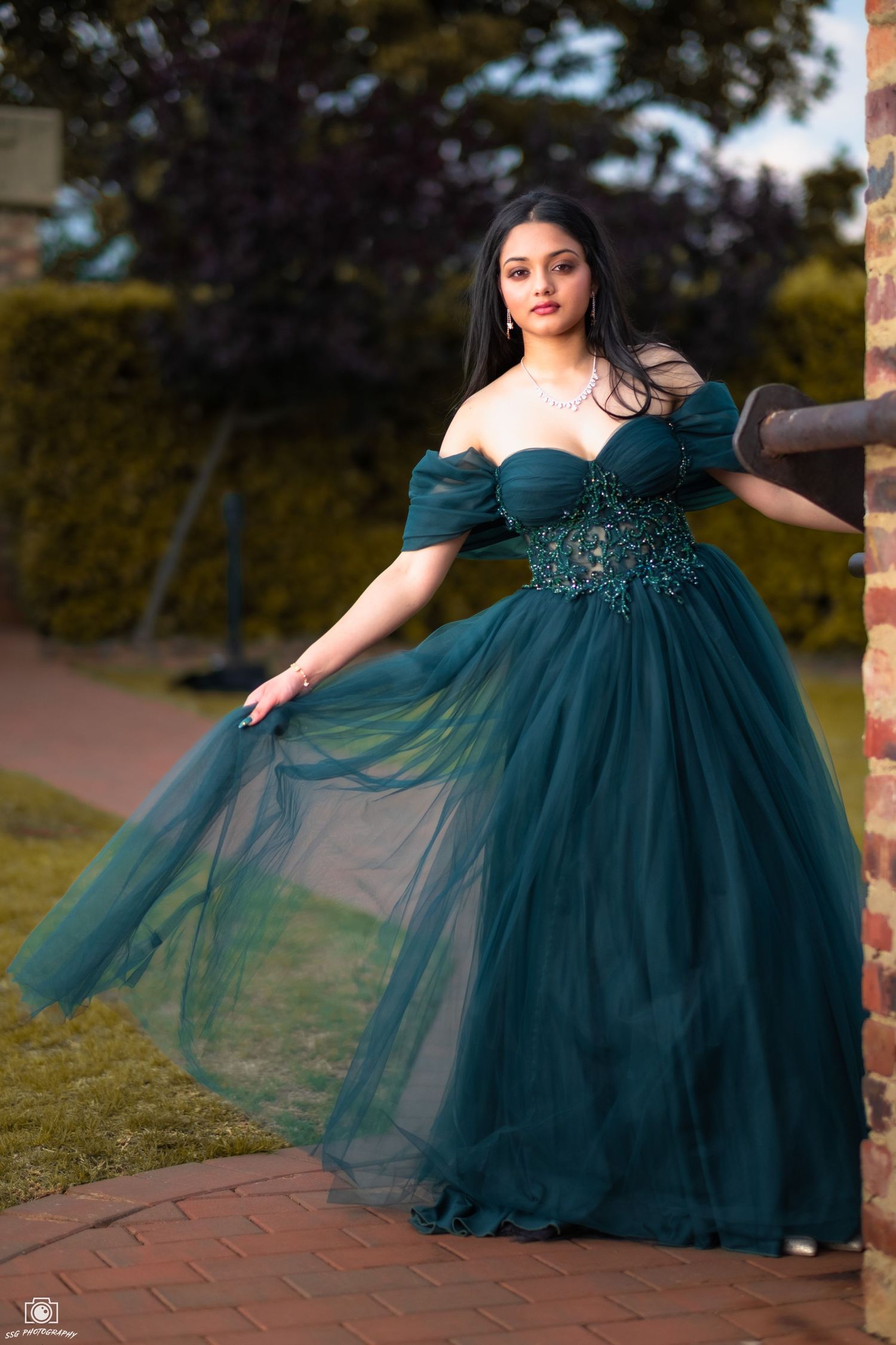 Flowing teal ball gown with tulle skirt captured in an outdoor garden setting.