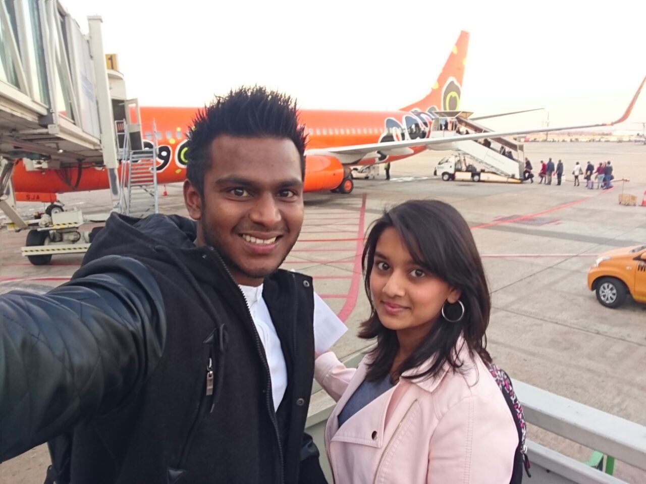 People posing near an orange airplane on an airport tarmac.
