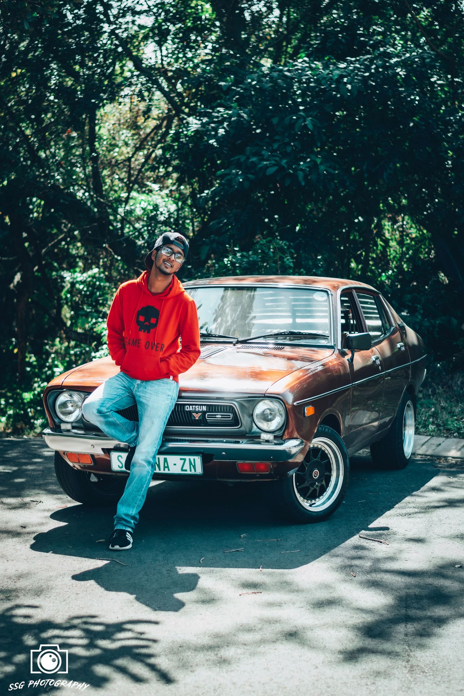 A vintage car photoshoot featuring a classic automobile with someone posing alongside it.